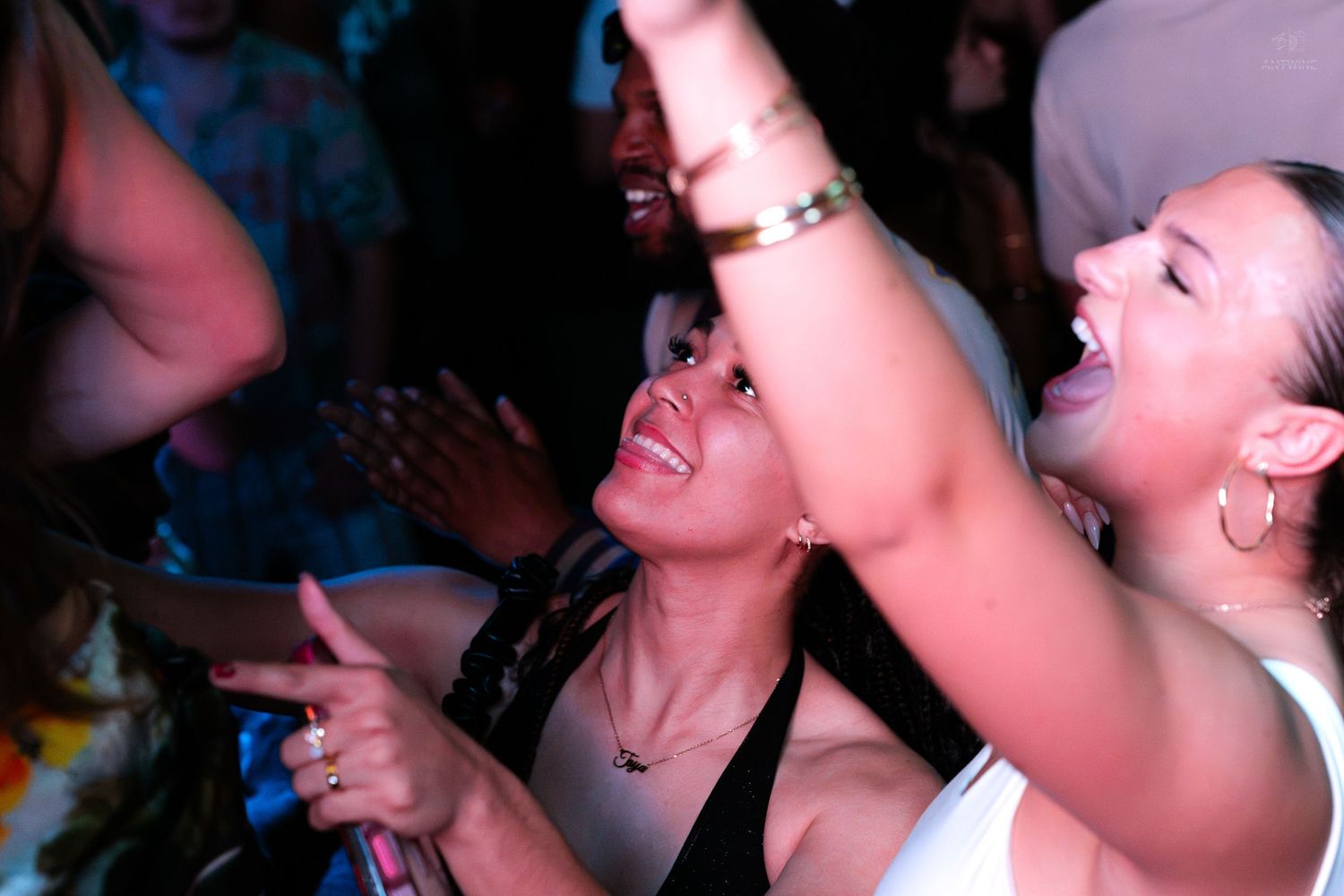 Two women laughing and dancing joyfully together at a lively nightclub party.