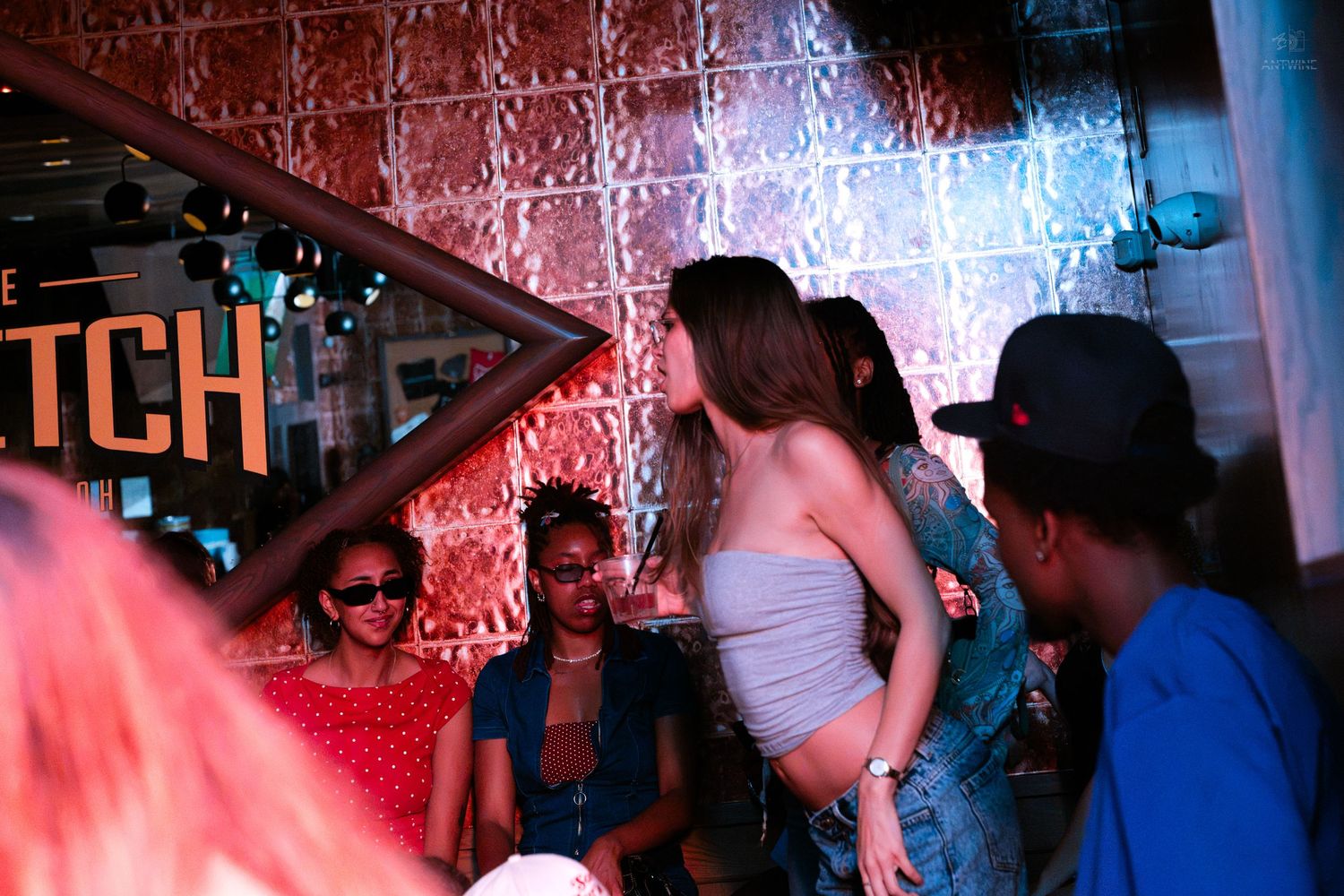 Group of people socializing under pink neon lights at a bar.