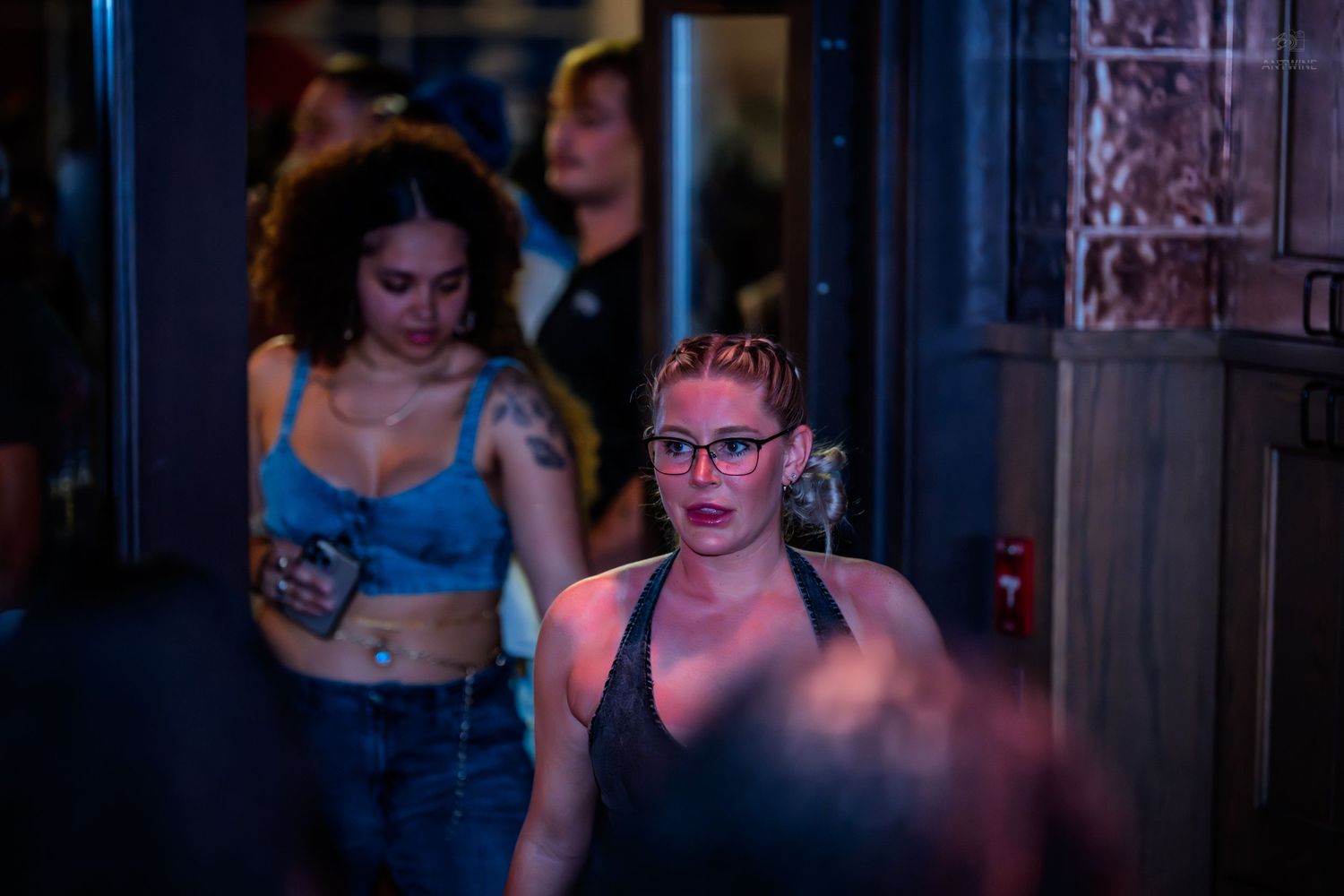 Two young women walking through a nightclub entrance under blue and purple neon lighting.