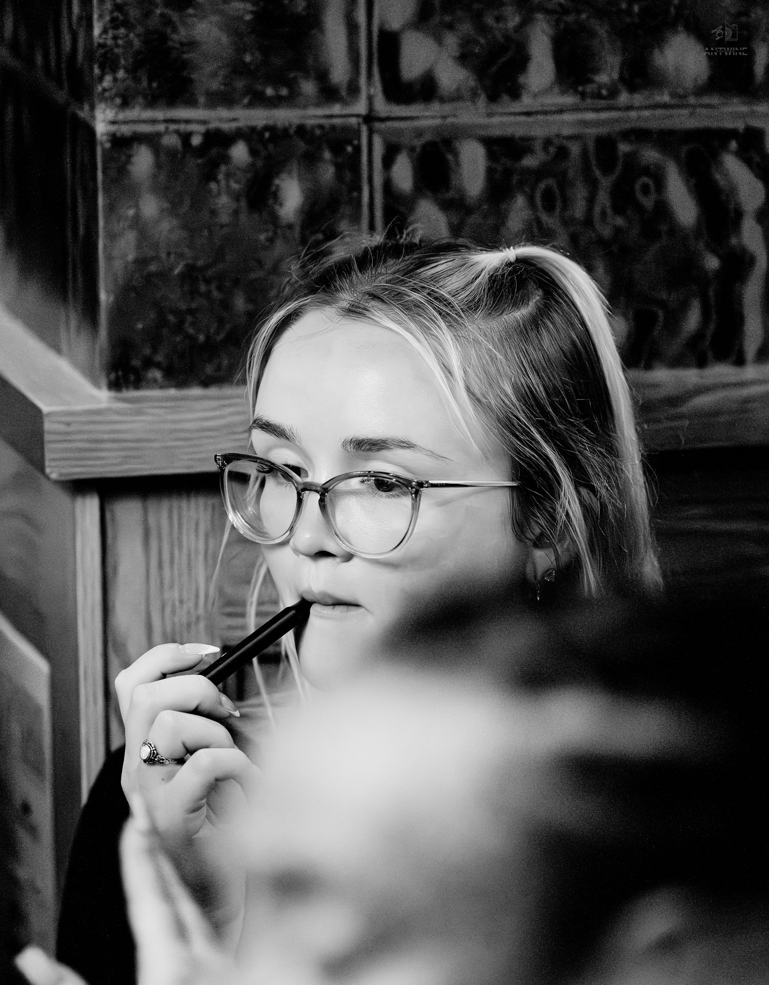 Young blonde woman with glasses vaping in colorful neon-lit bar environment, side profile view.
