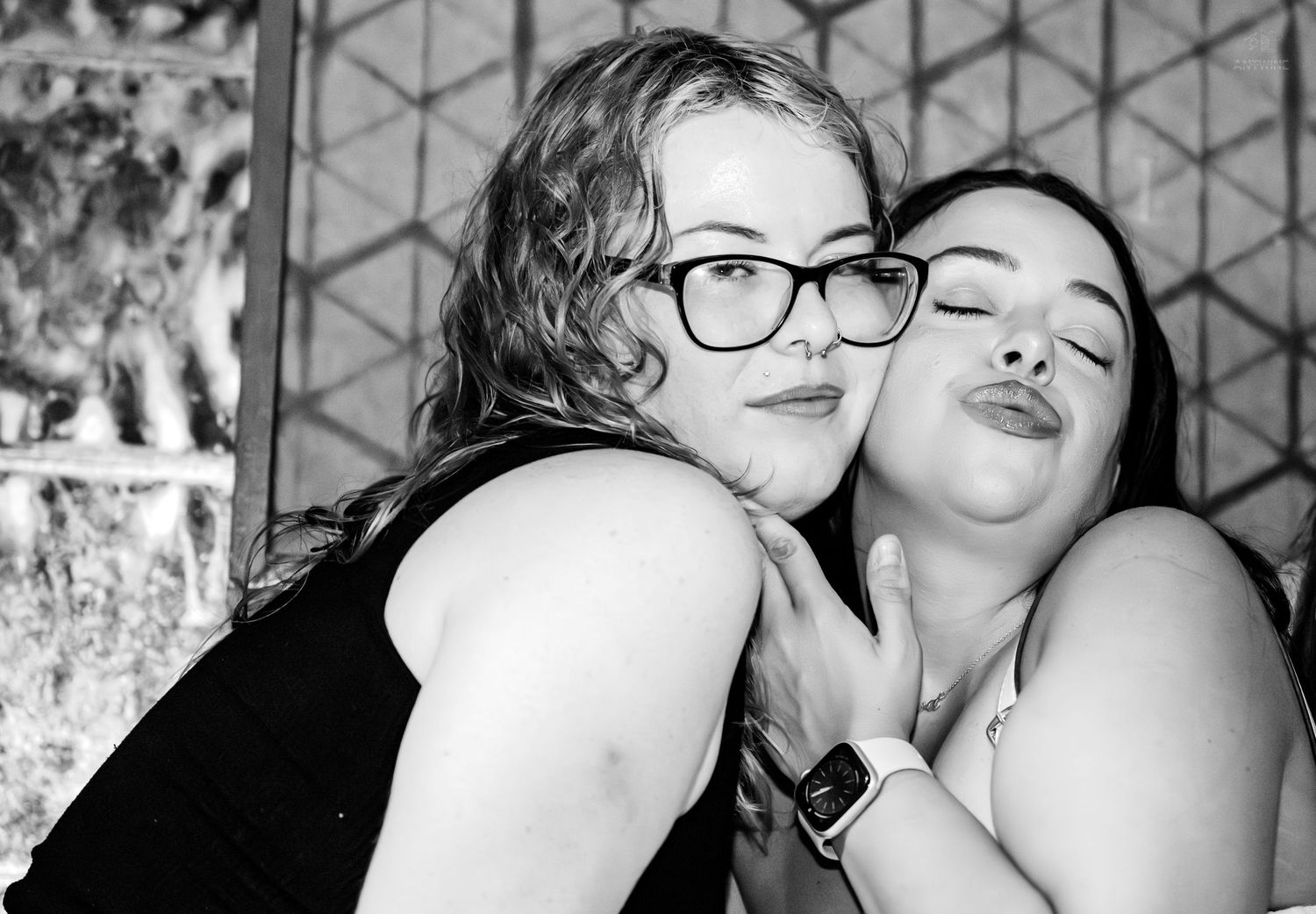 Two friends pose playfully together in black and white photo at a bar.