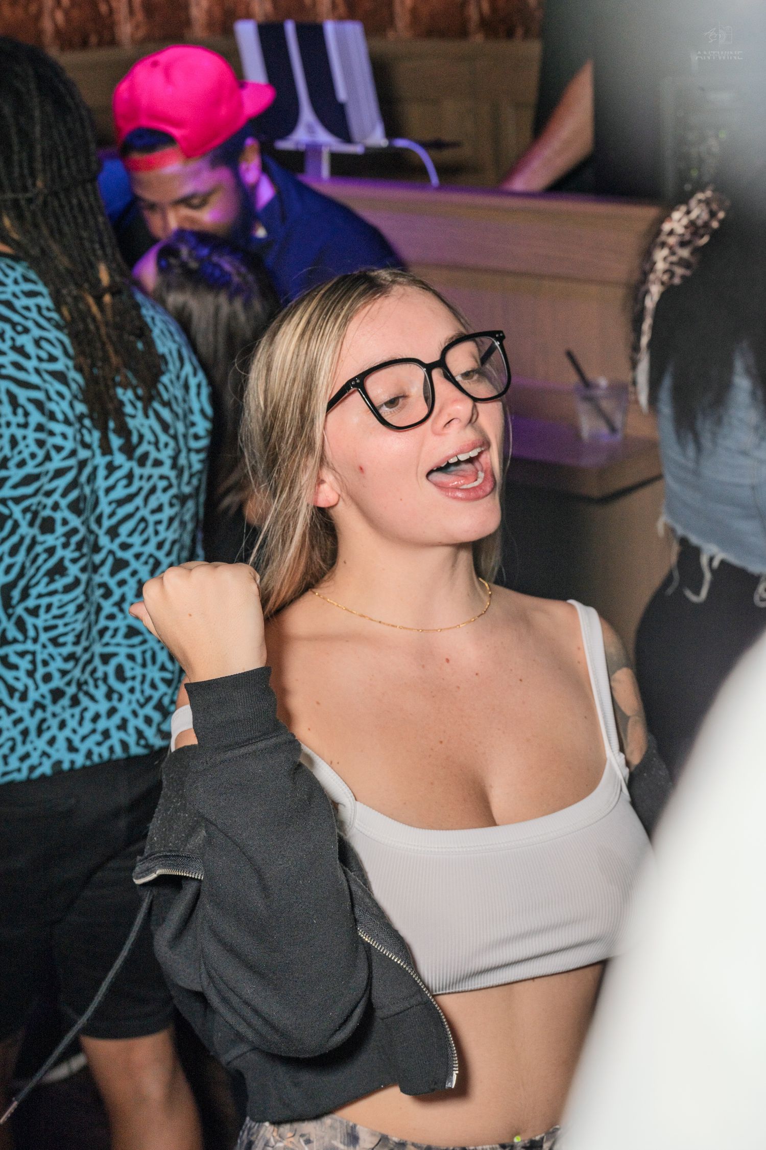 Blonde woman with black glasses singing and dancing at a vibrant nightclub party.