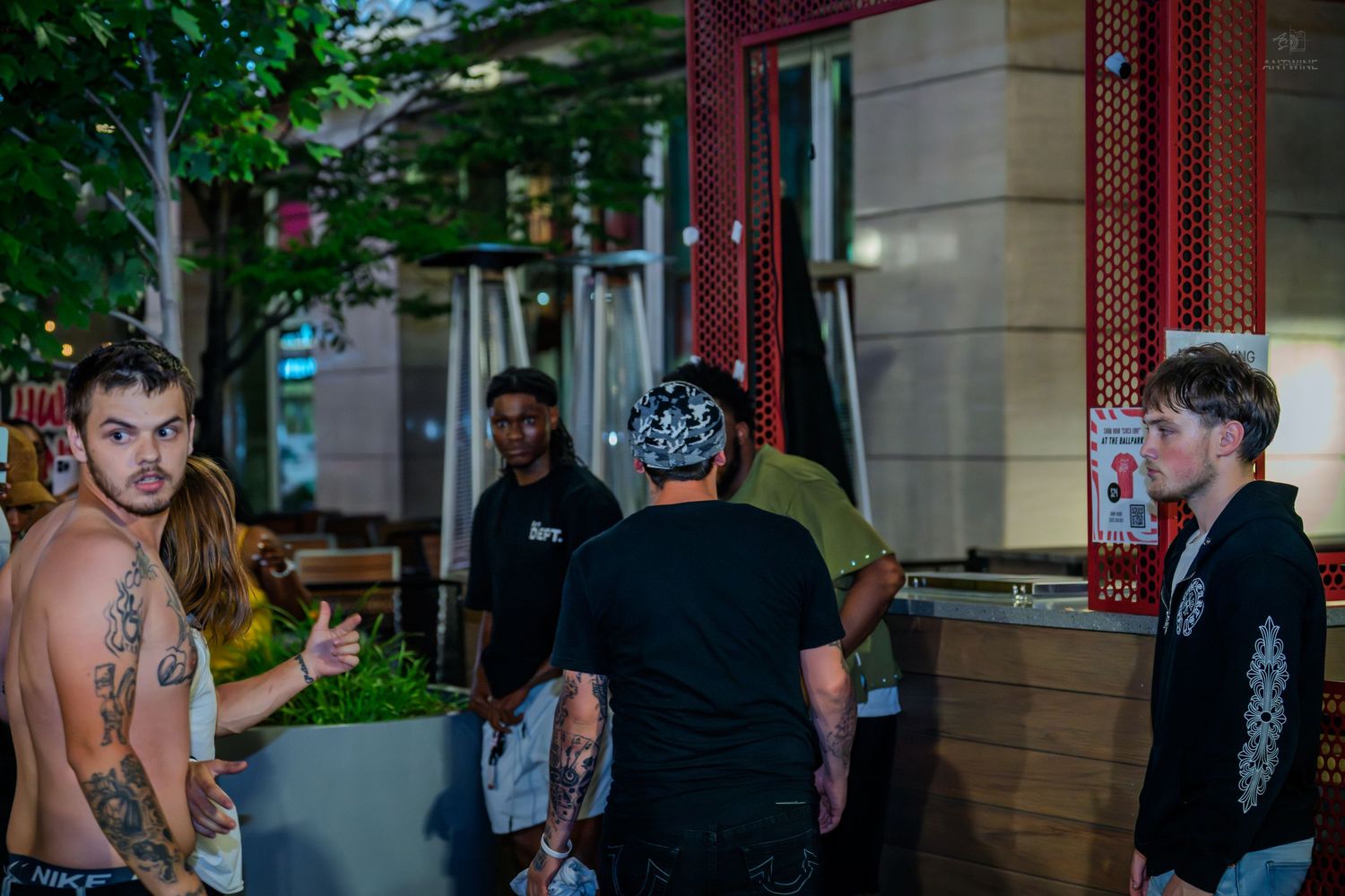 Tattooed shirtless man and friends outside urban restaurant at night.