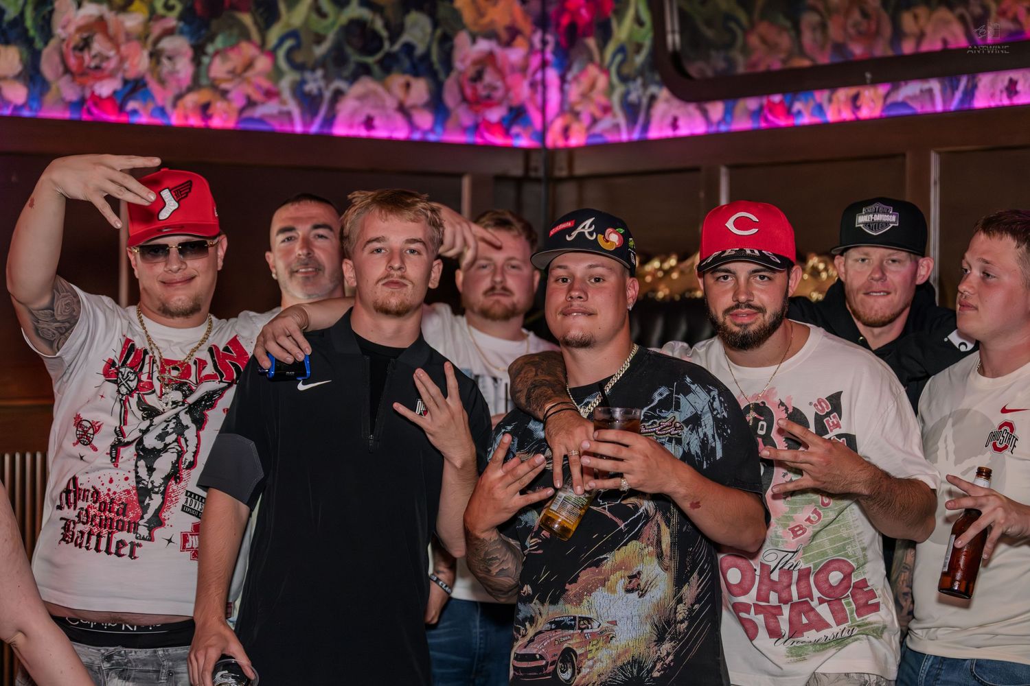 Group of young men gathered together smiling at a vibrant nightclub with neon lights.