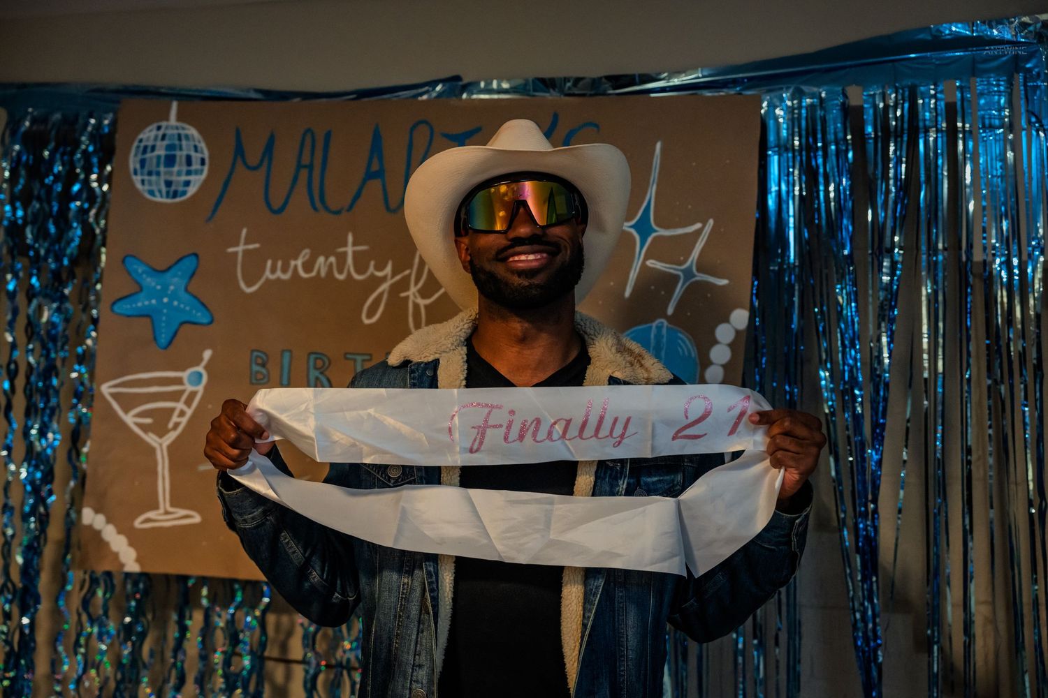 Man in white cowboy hat and sunglasses holds a Finally 21 sash at Malarie's birthday party.