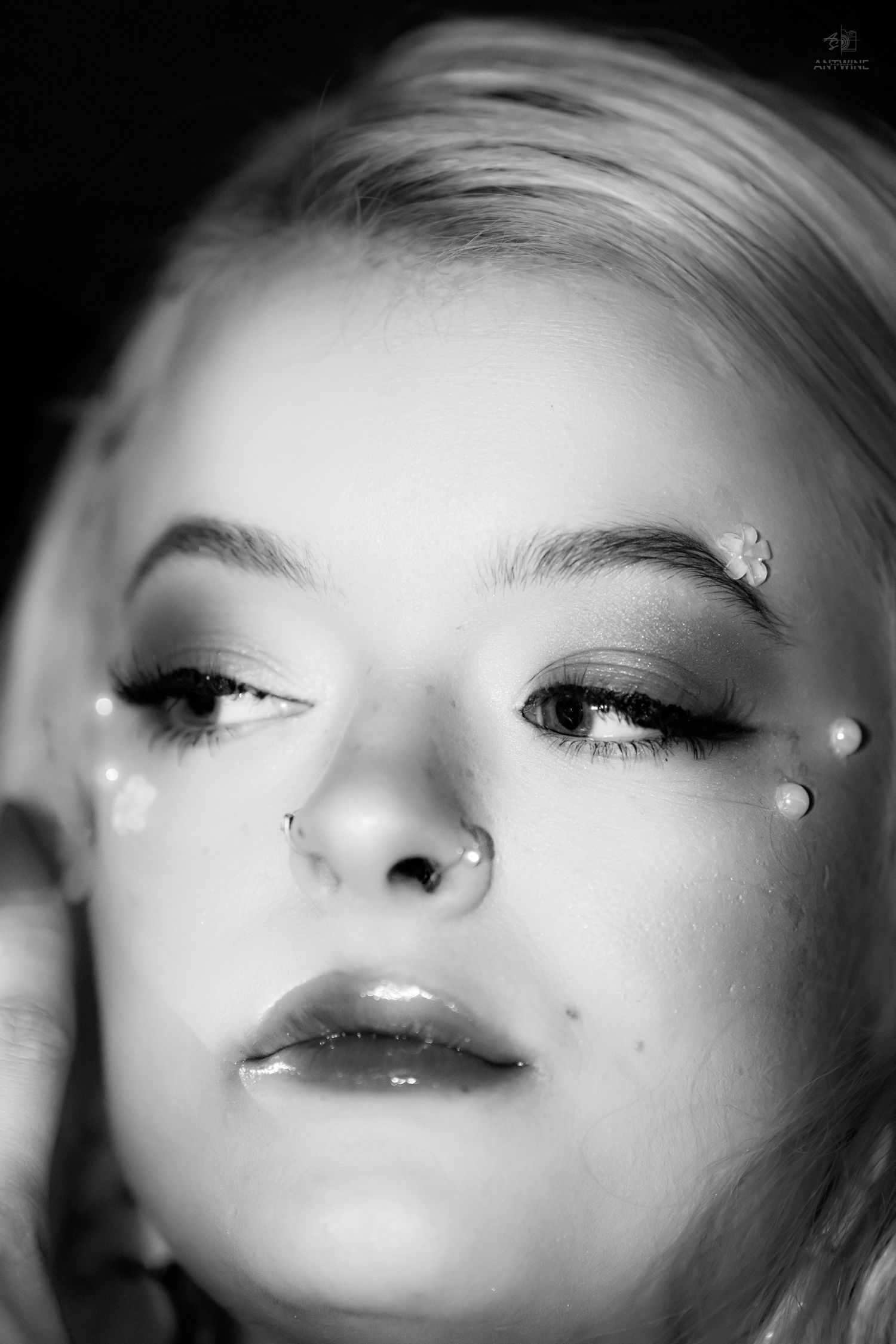 Black and white close-up portrait of blonde woman with pearl face gems, nose ring, and glossy lips.