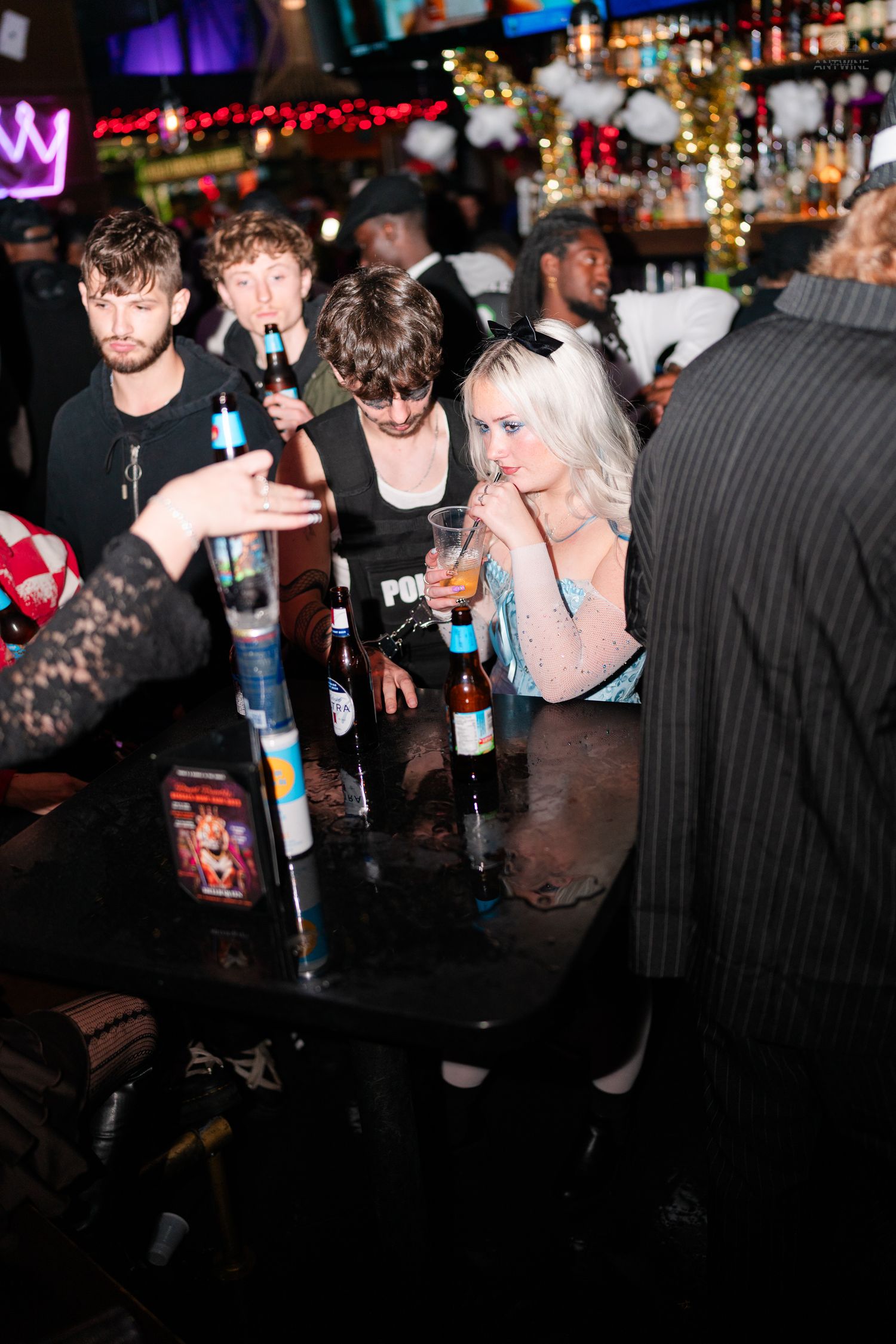 People socializing at a dimly lit bar with beer bottles on a table.