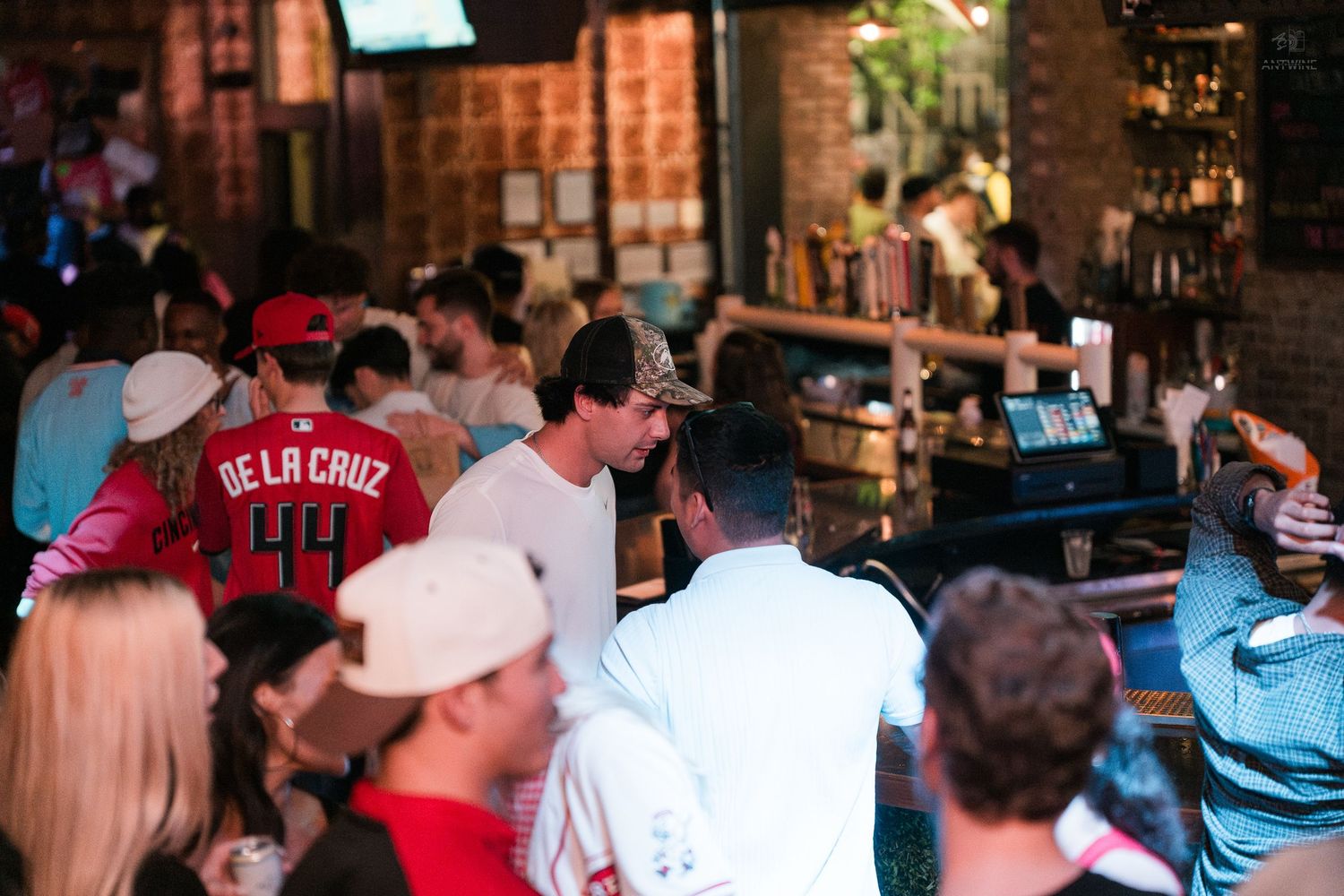 Crowded sports bar with fans wearing Cincinnati Reds jerseys gathered near the counter.