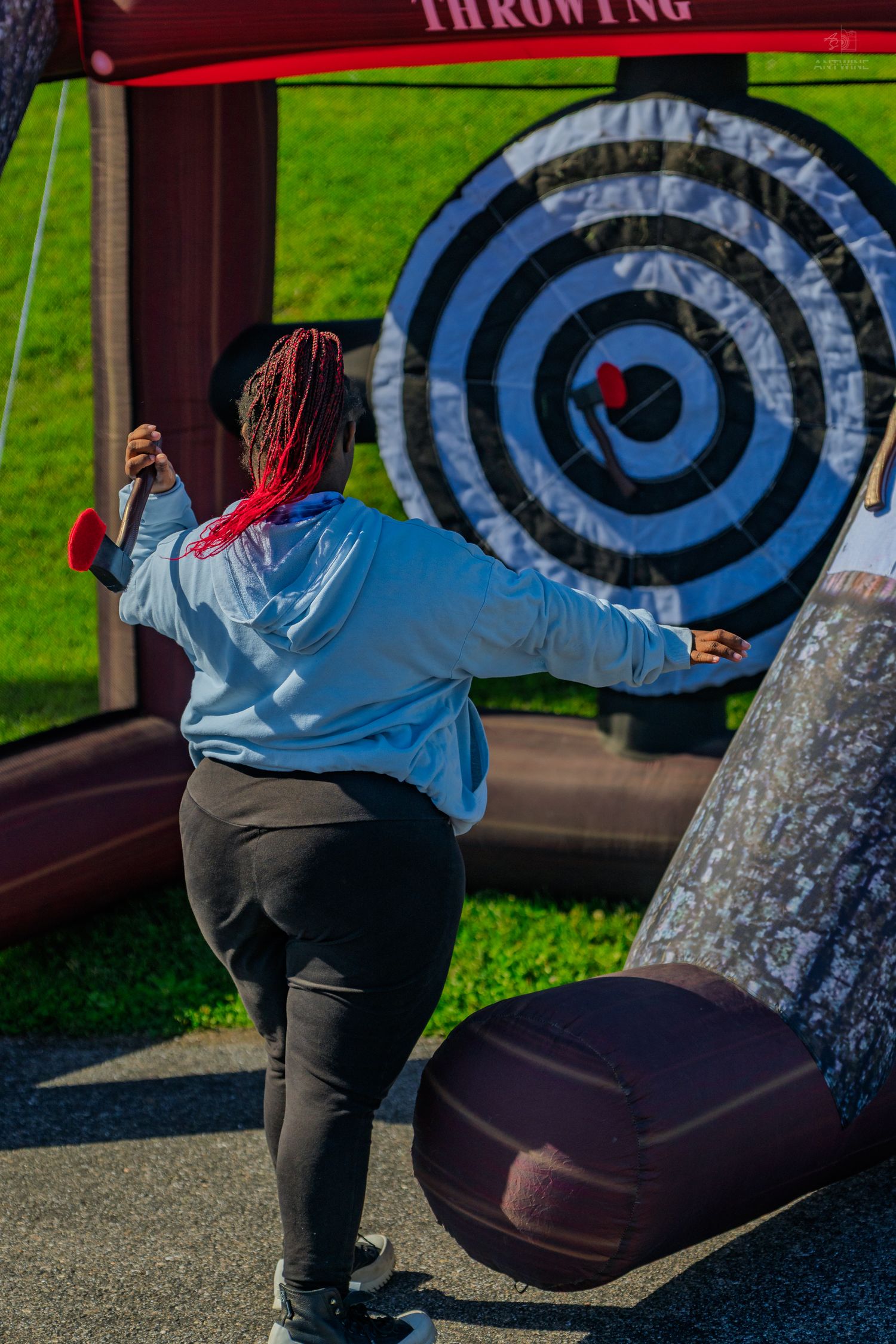 Woman throwing an axe at a large inflatable bullseye target at an outdoor axe throwing activity event.