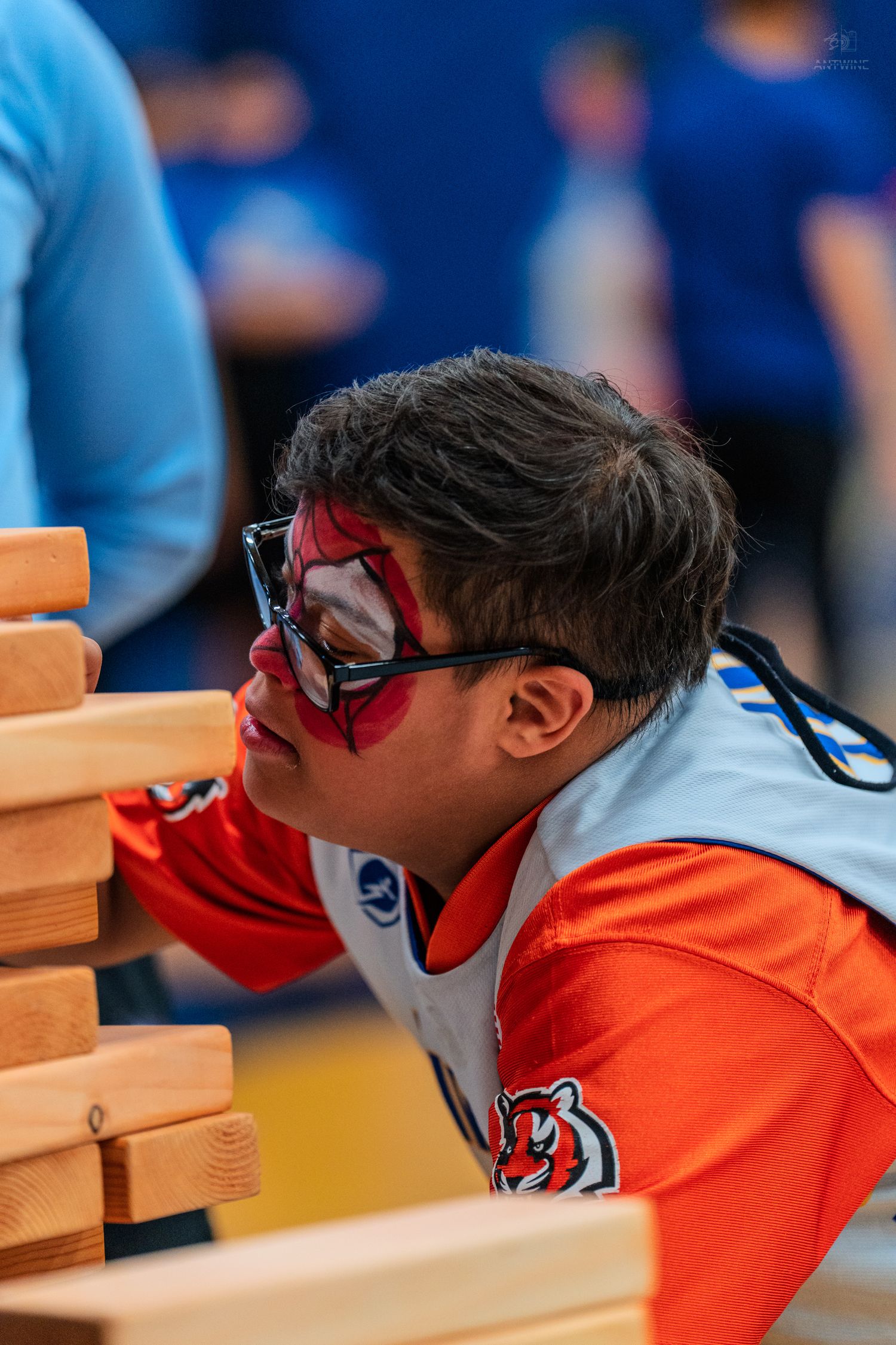 Boy with Spider-Man face paint plays giant Jenga in a Cincinnati Bengals jersey at an indoor event.