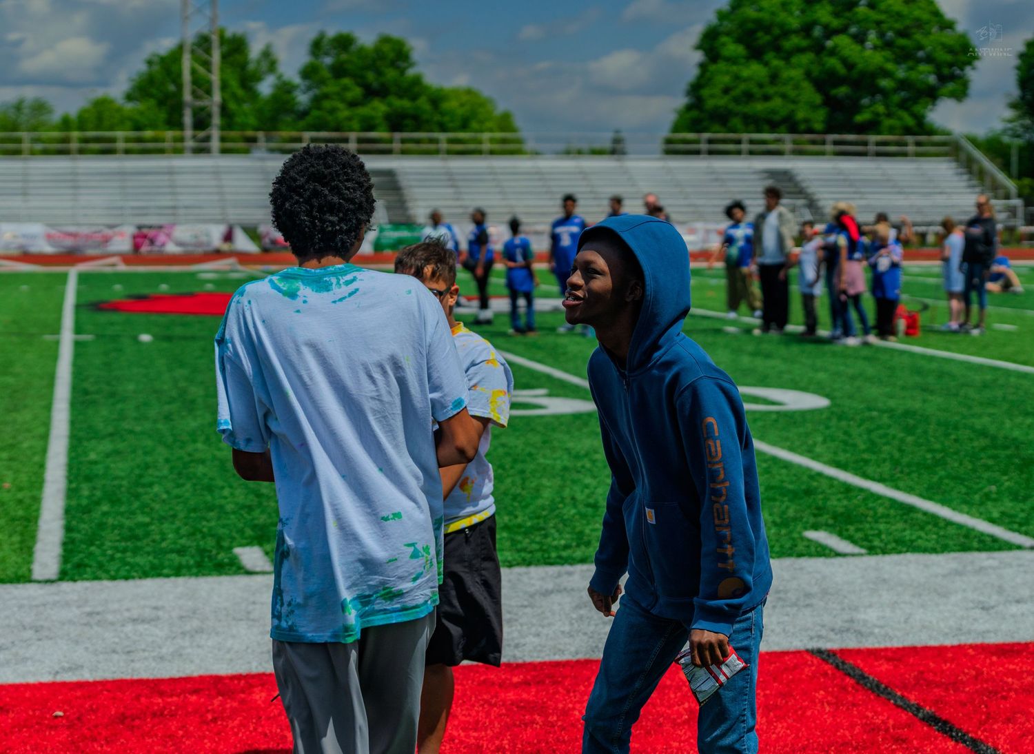 Young athletes socializing on a red track field at an outdoor sports event on a cloudy day.