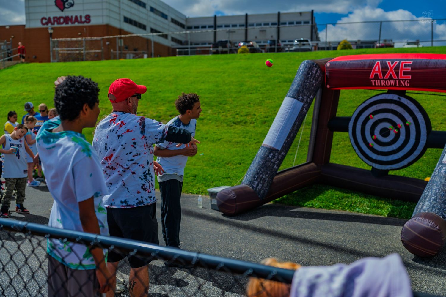 Kids playing inflatable axe throwing game at Cardinals outdoor event on sunny day.