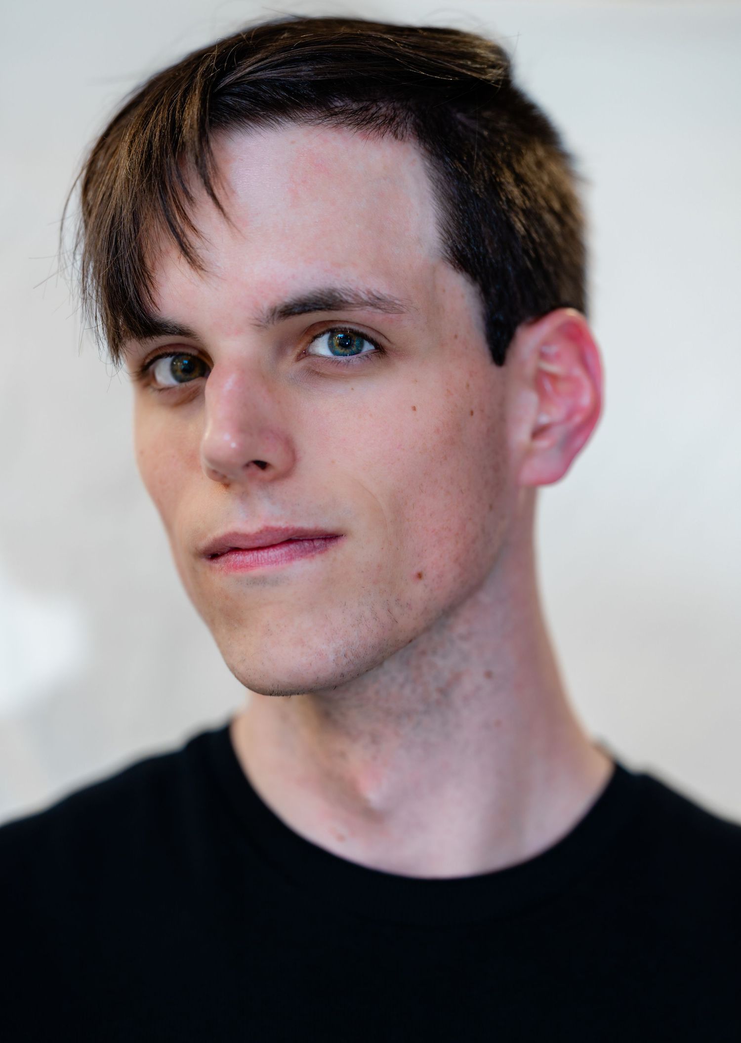Young man with dark hair and light eyes in a black t-shirt poses for a professional portrait photo.