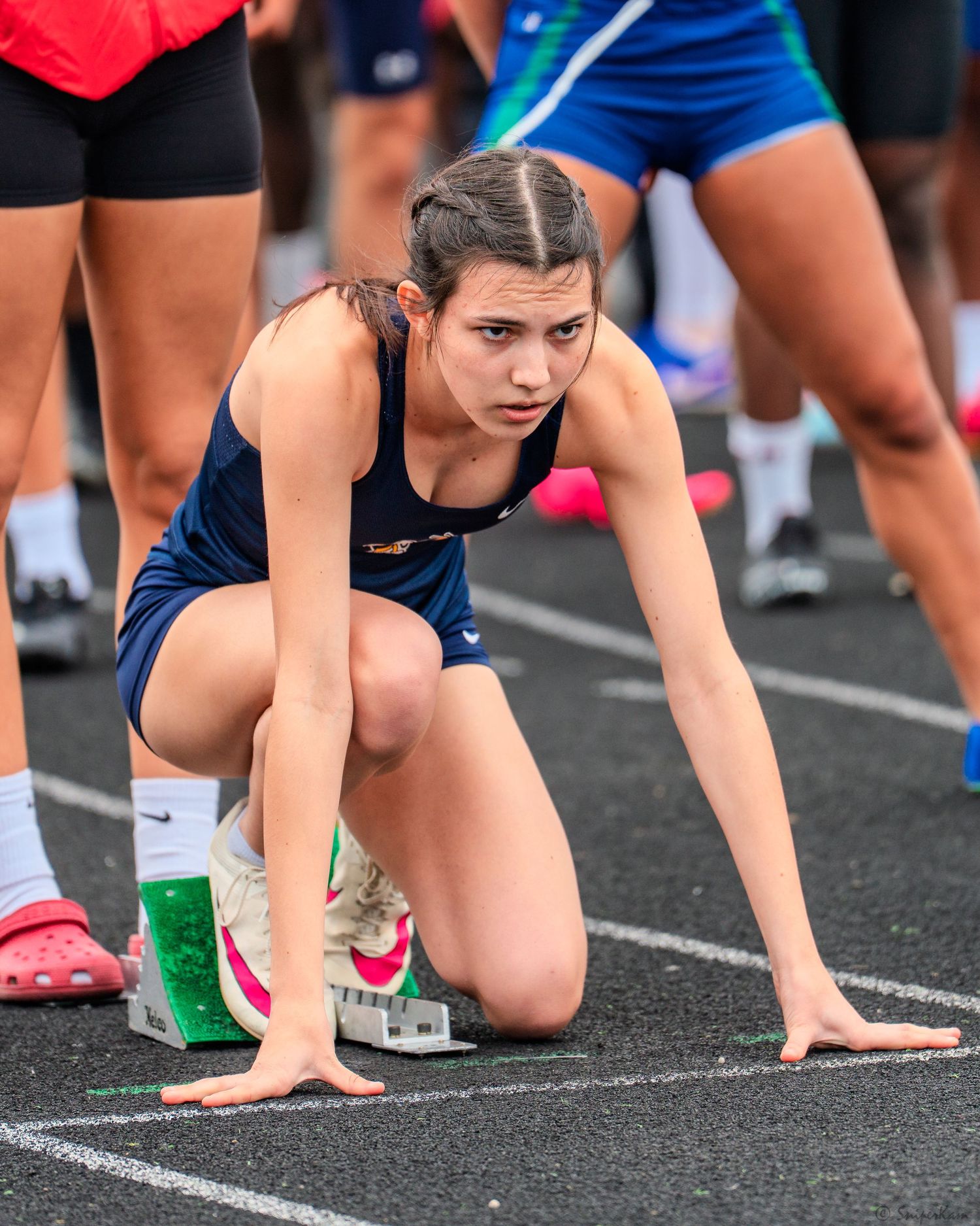 Female sprinter in navy uniform crouched in starting position on track blocks ready to race.