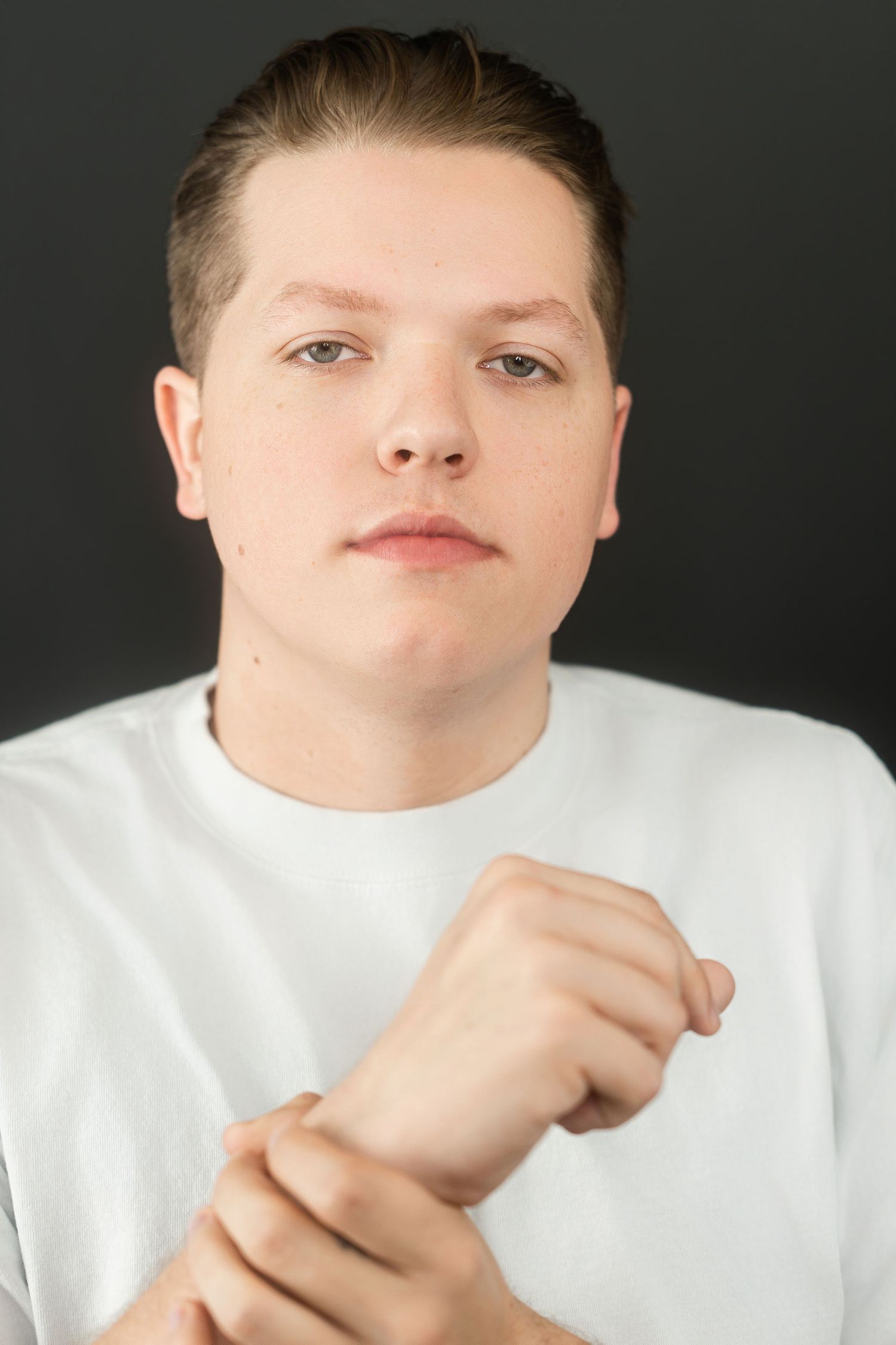 Young man in white t-shirt gripping wrist with both hands, serious expression, dark background.