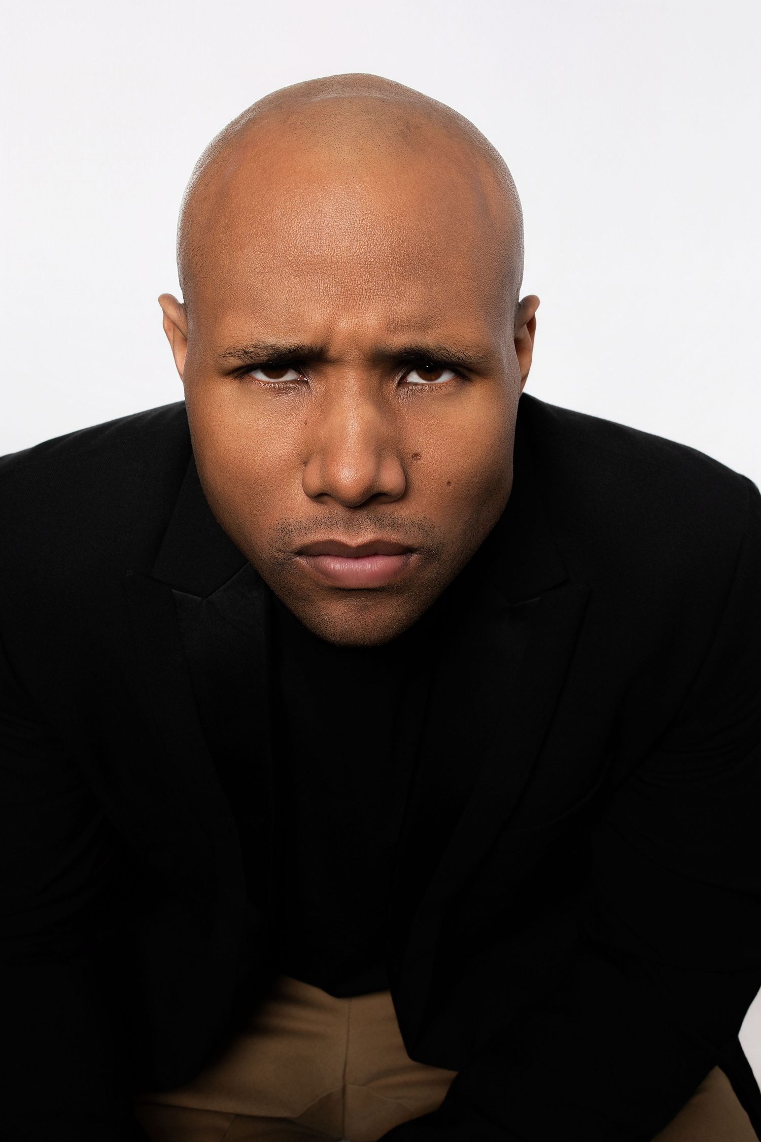 Bald Black man in black blazer frowning with intense expression in studio portrait photo.