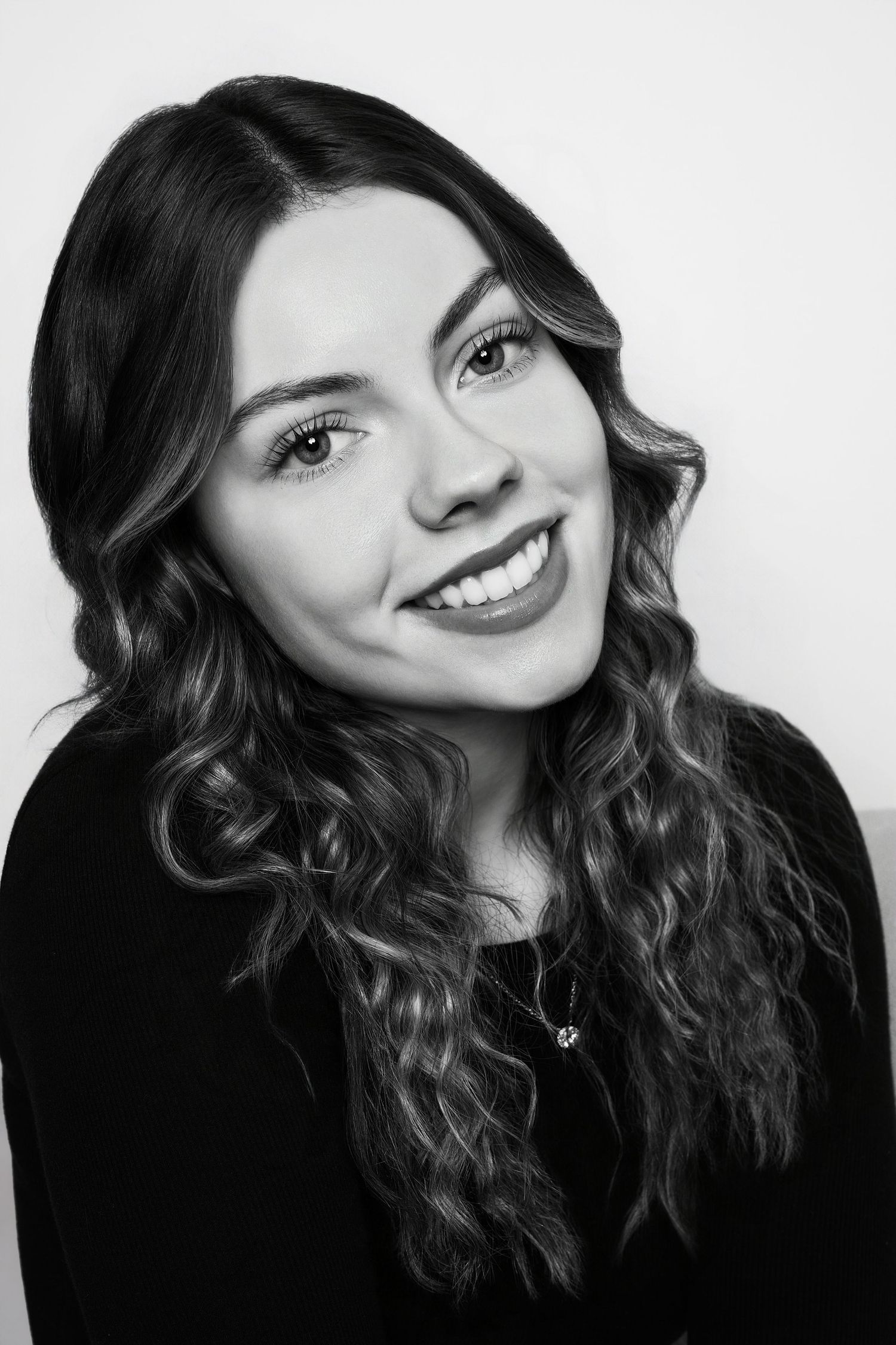 Black and white headshot of a smiling young woman with long curly hair and a delicate necklace.