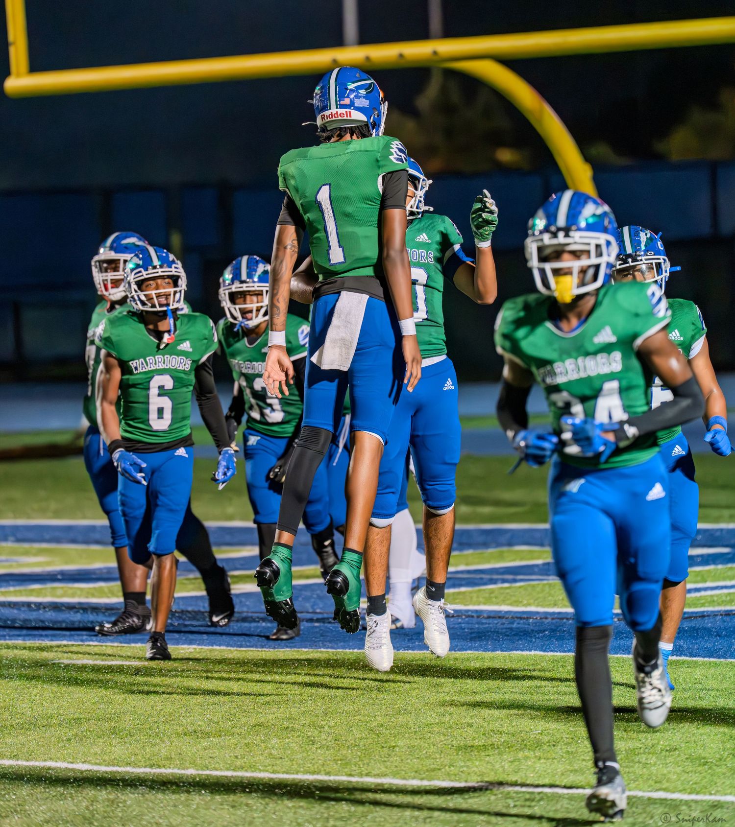 Warriors football players in green and blue celebrate with player number 1 after a scoring play.