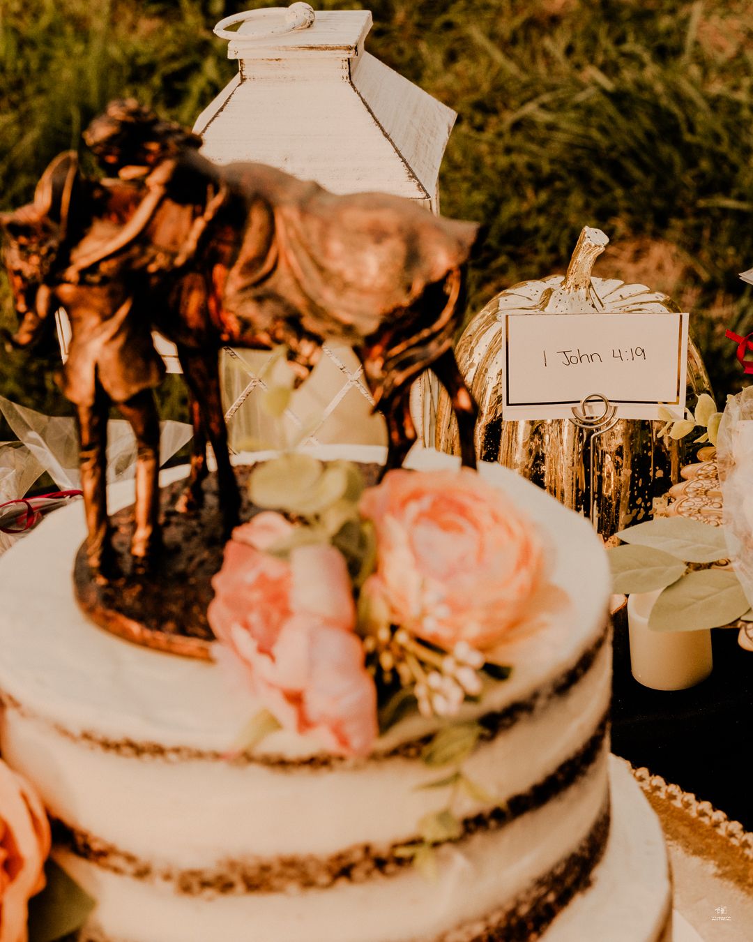 Rustic naked wedding cake with horse topper, pink flowers, and 1 John 4:19 scripture card display.