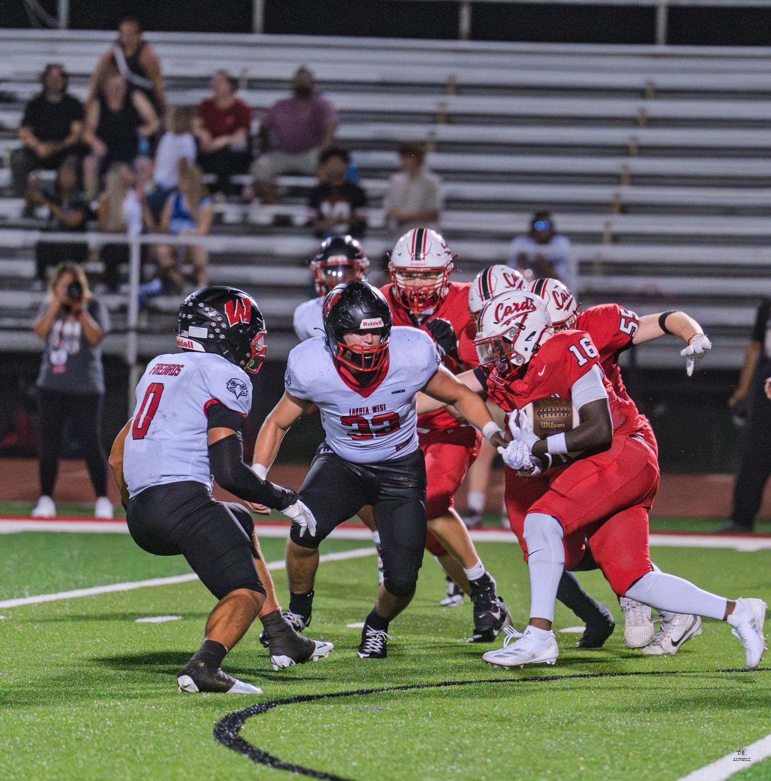 Red and white football teams clash at line of scrimmage during an intense high school game.