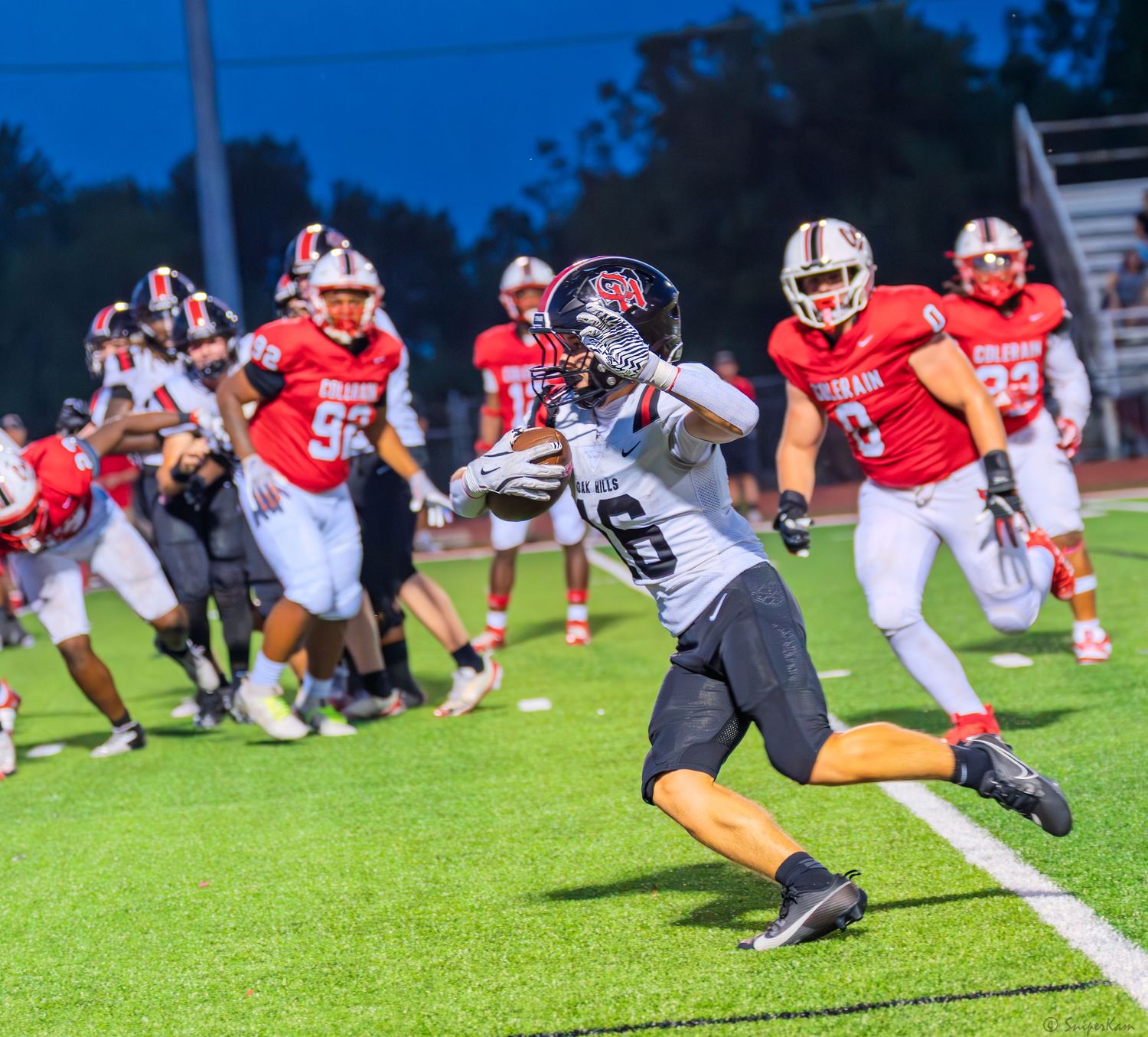 Football player in dark uniform runs along the sideline while Colerain defenders give chase.