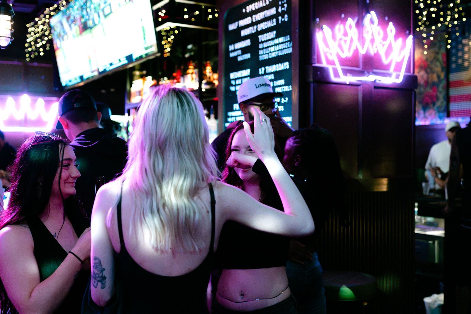 Blonde woman taking photos at a neon-lit nightclub with glowing crown sign.