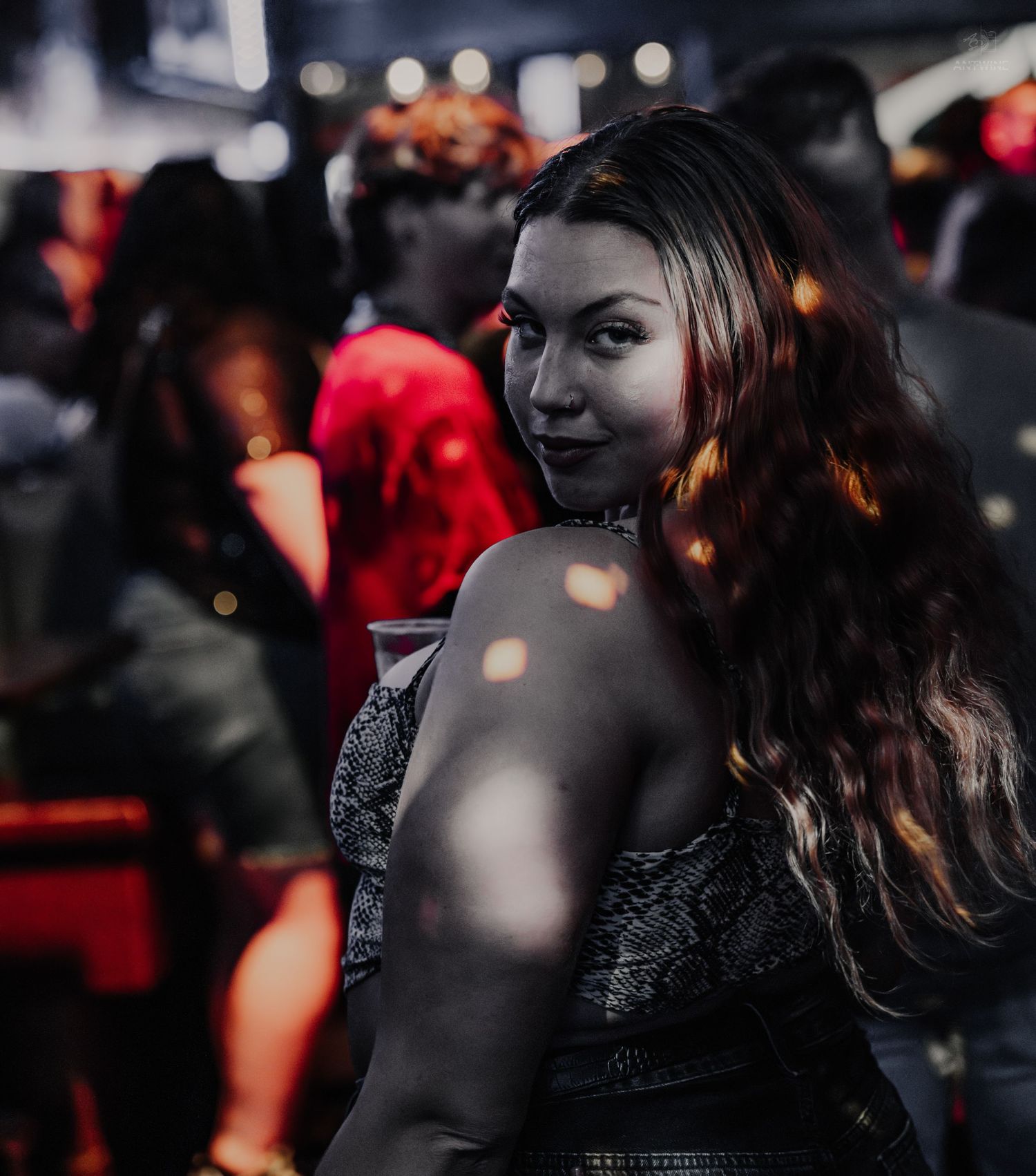Woman with long wavy hair glancing back at camera in a dimly lit nightclub.