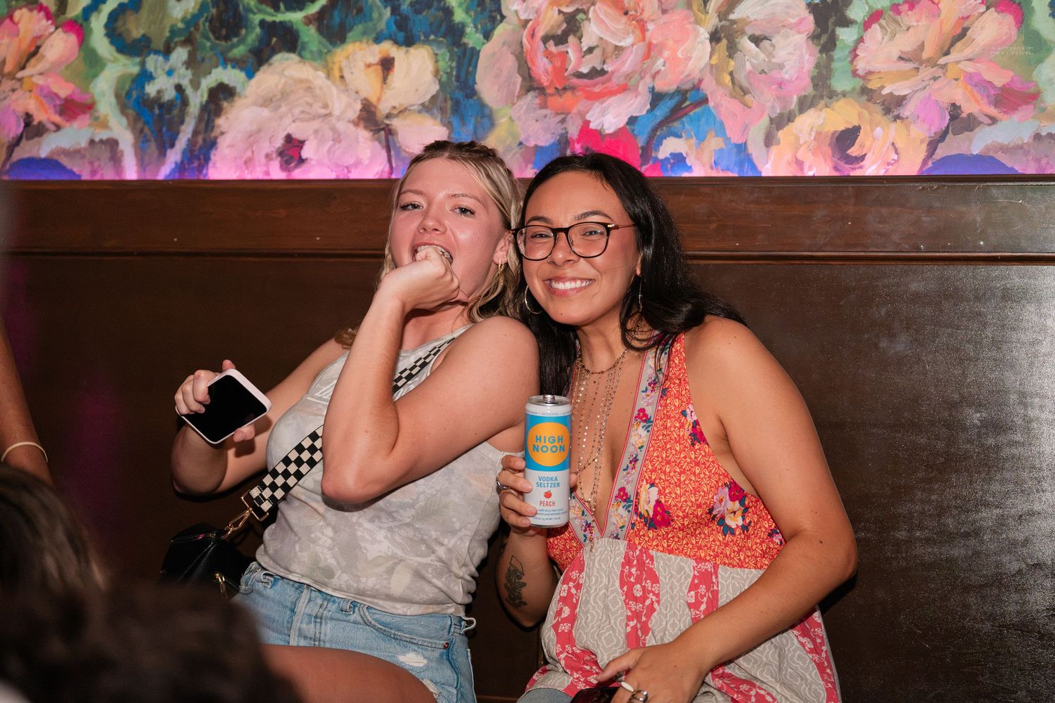 Two smiling women posing together at a bar, one holding a canned beverage.