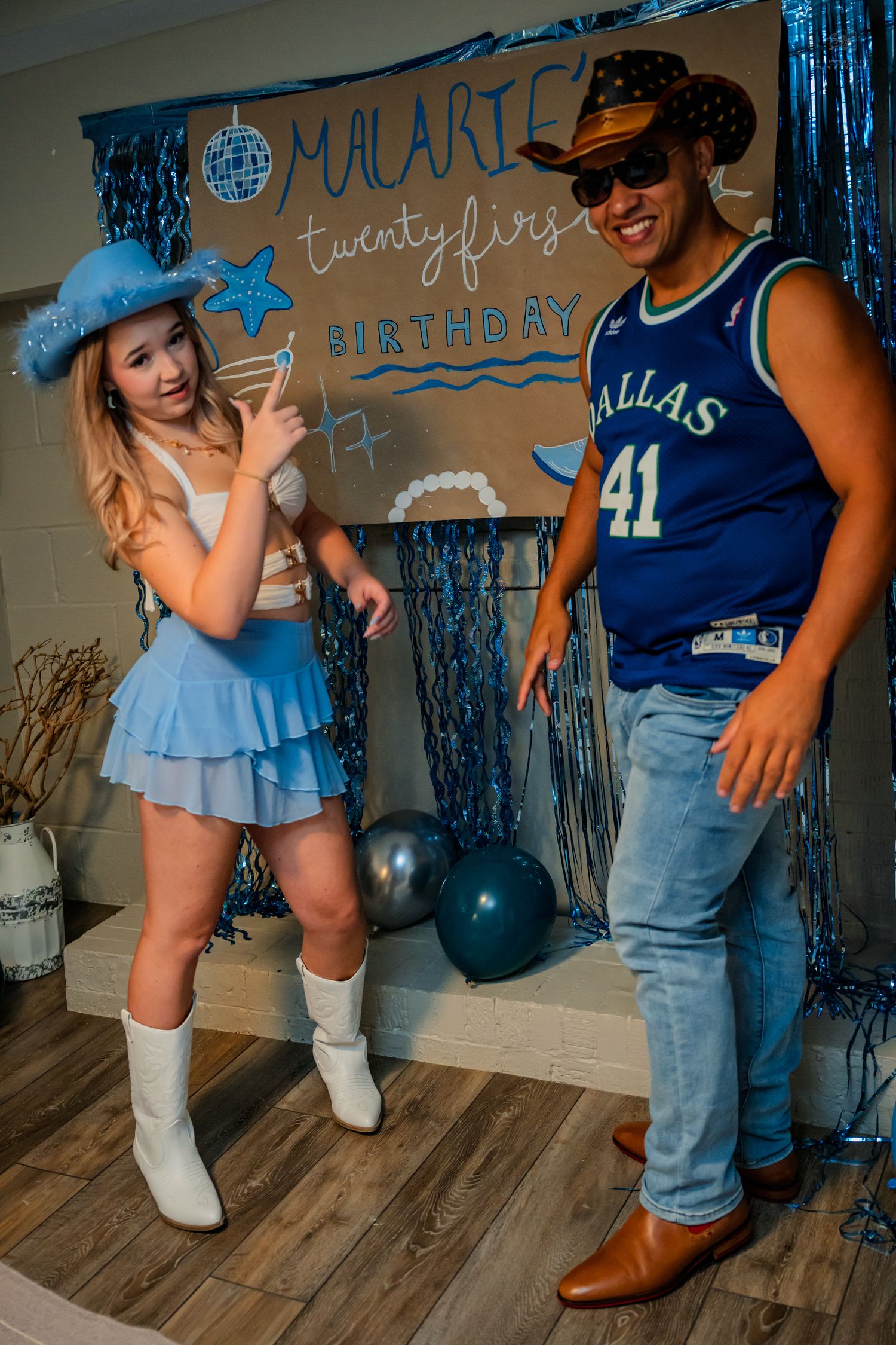 Two friends point and smile at Malarie's 21st birthday party with blue balloon decorations.