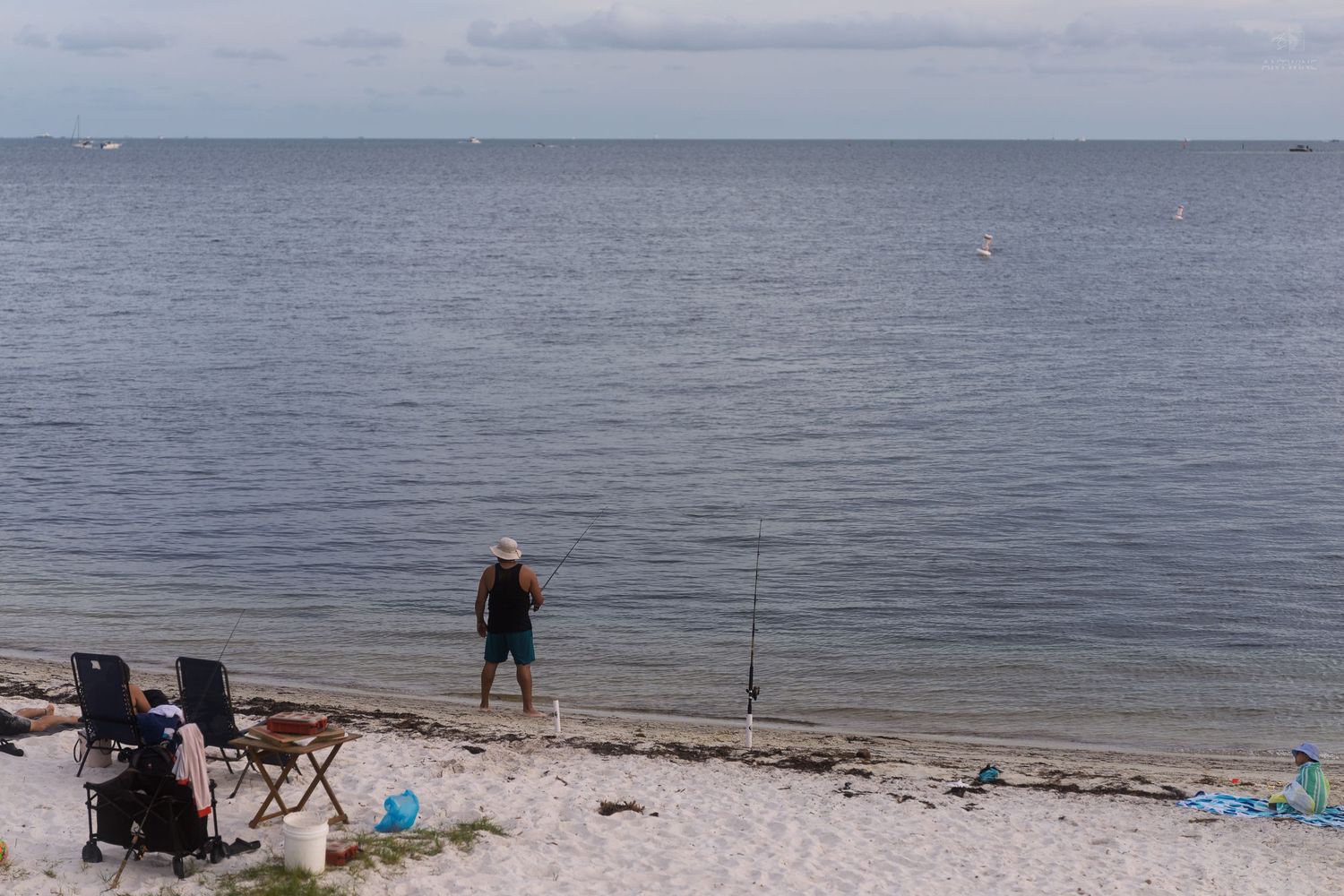 Lone fisherman standing on white sand beach with fishing rods and chairs at Key Biscayne, Florida.