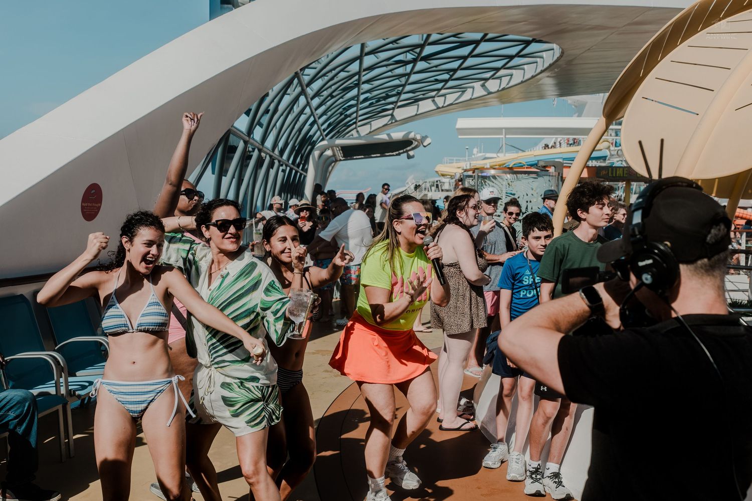 Energetic passengers dancing on a cruise ship deck while being filmed.
