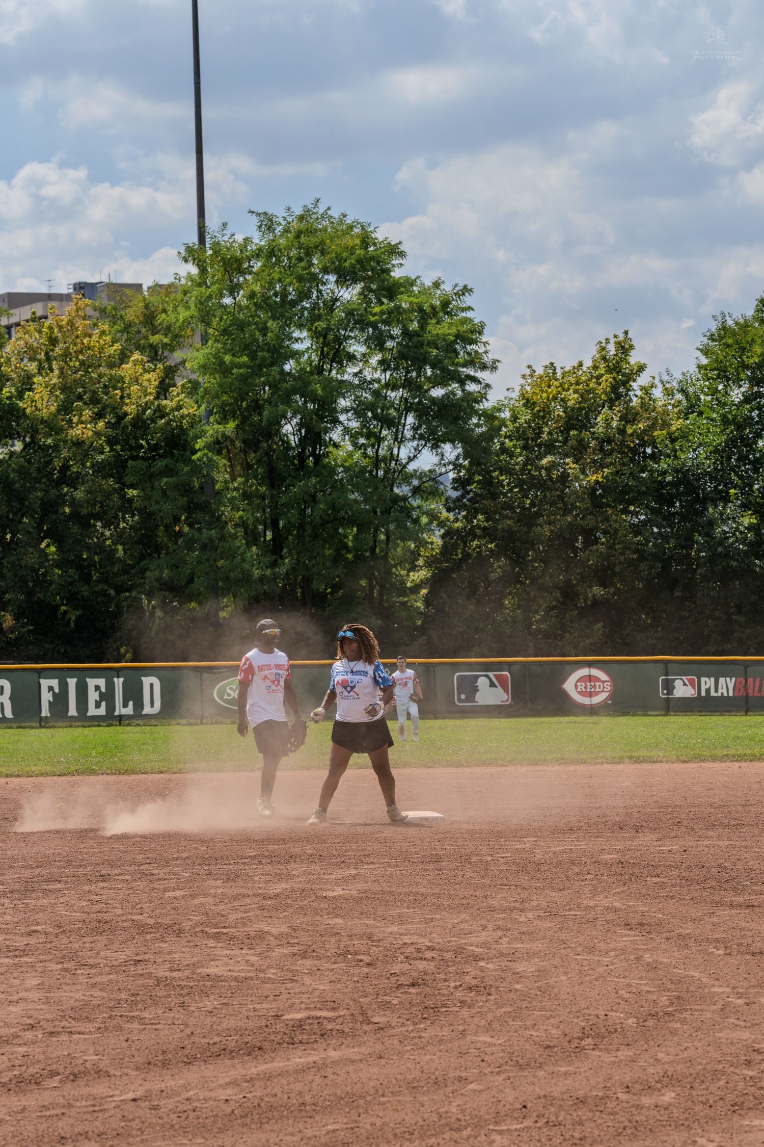 Two female softball players near second base kicking up dust during an outdoor recreational game.