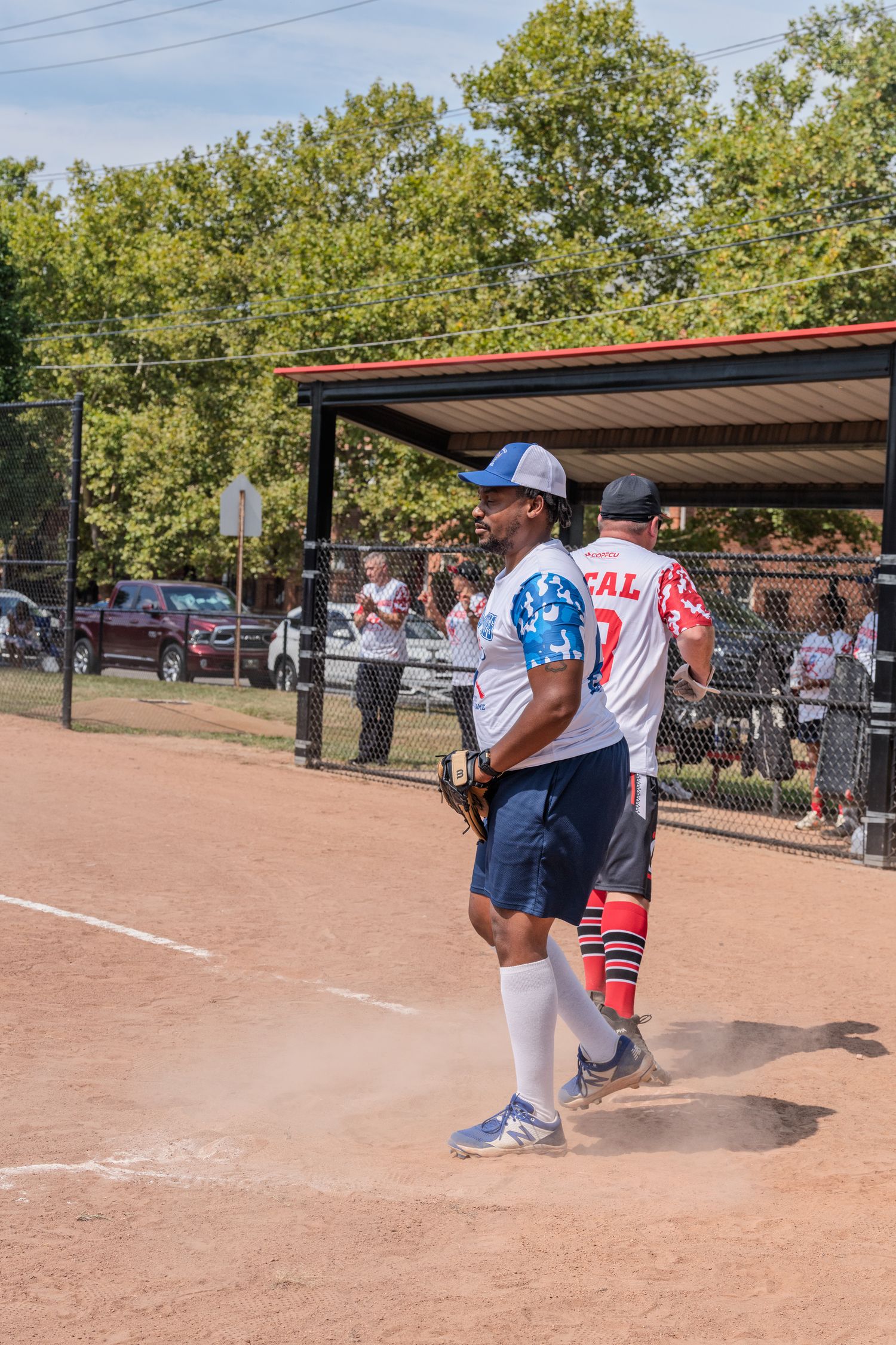 Two softball players walking near home plate during outdoor daytime game at park.