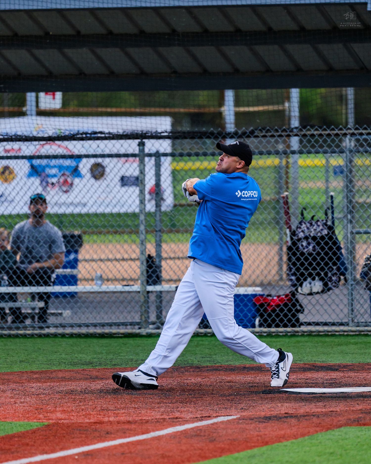 Softball player in blue COPFCU jersey swinging bat during an evening recreational league game at dusk.