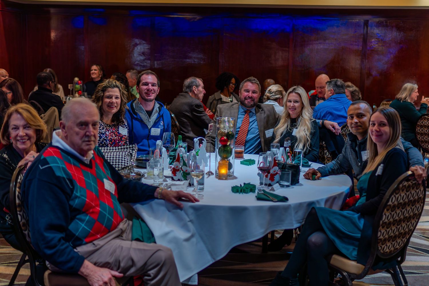 Group of smiling adults seated at a round table during a festive holiday dinner party event.