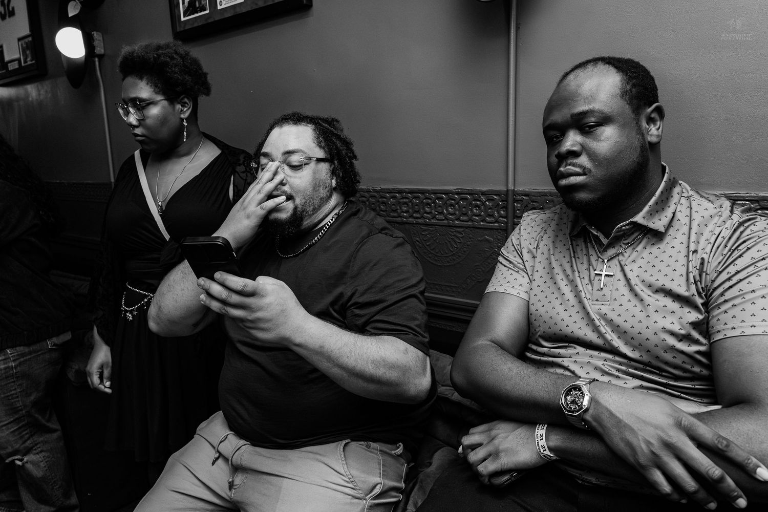 Black and white photo of three people sitting together, one looking at a phone in a dimly lit room.