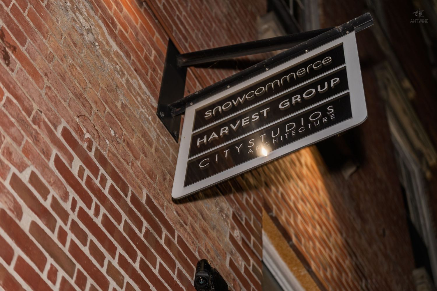 Snowcommerce Harvest Group City Studios sign mounted on a brick wall at night.