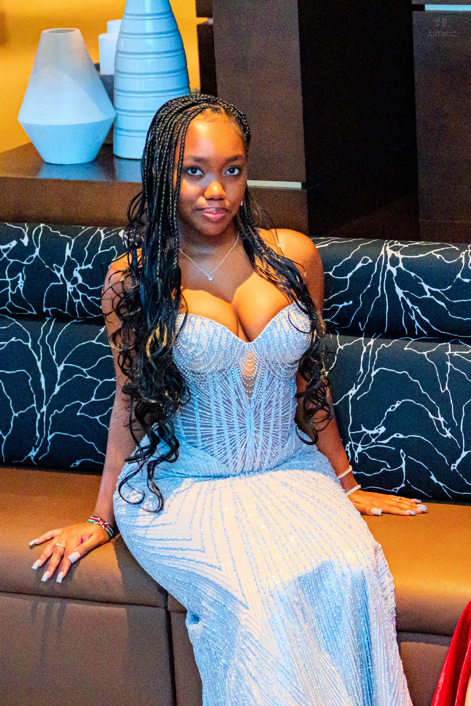 Young woman in a sparkling blue strapless corset gown with long braided hair seated on a sofa.