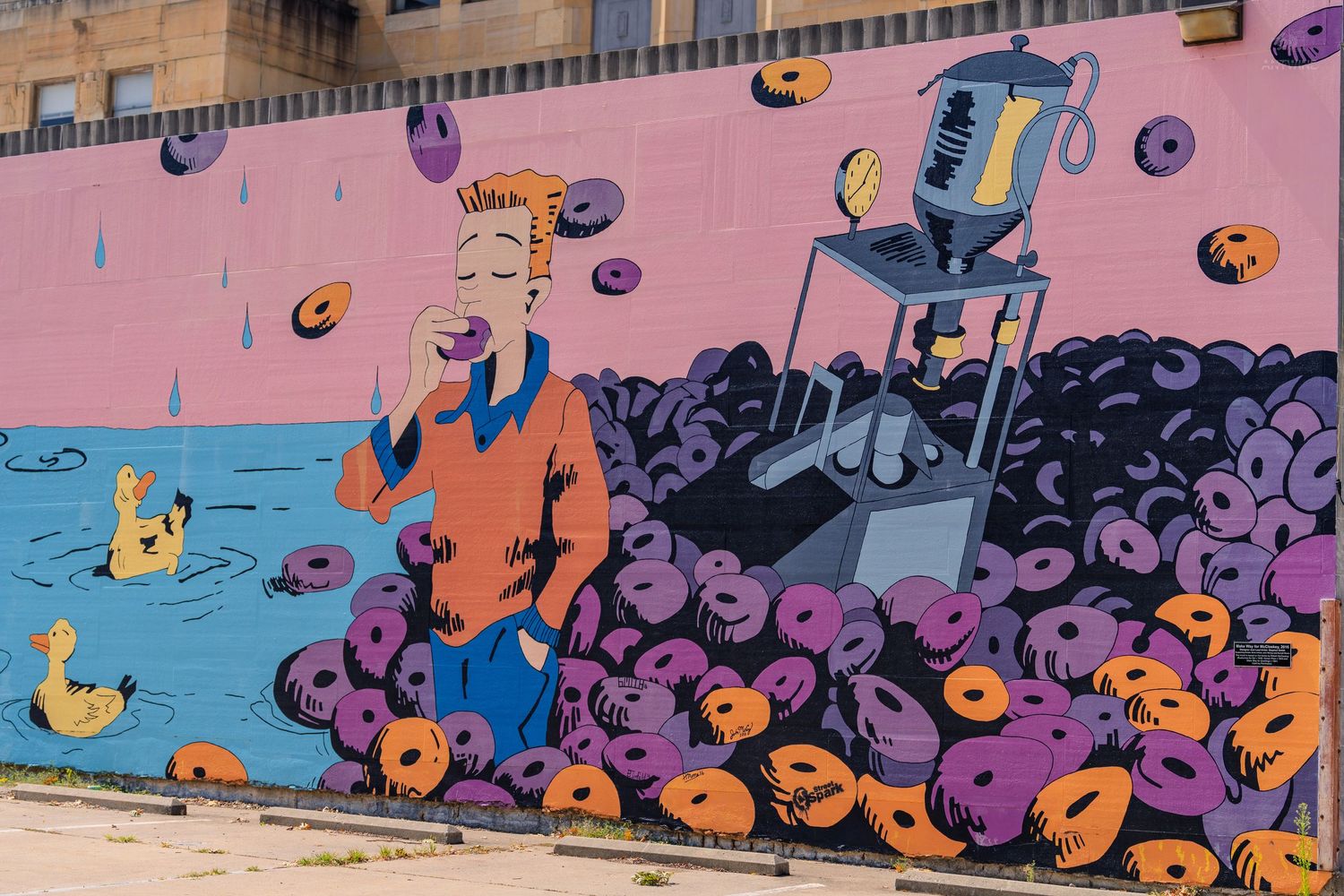 Colorful street mural featuring a cartoon figure surrounded by purple and orange donuts with a coffee machine on a pink wall.