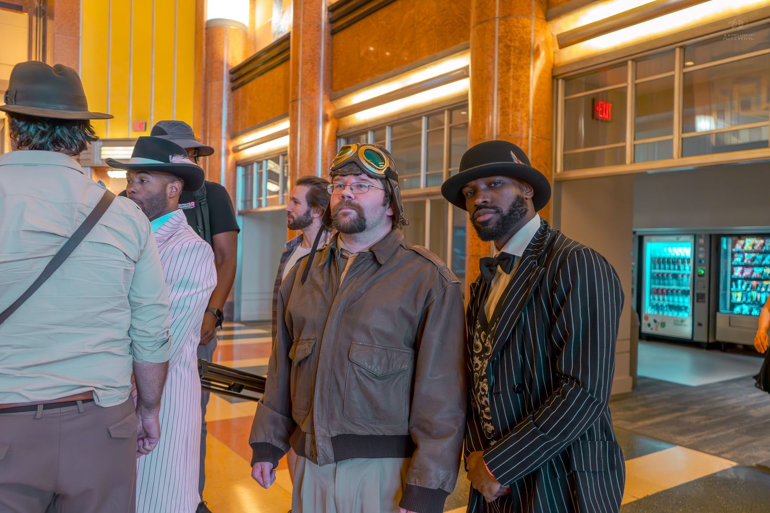 Men in vintage steampunk costumes including aviator jacket and zoot suit gather in a modern lobby.