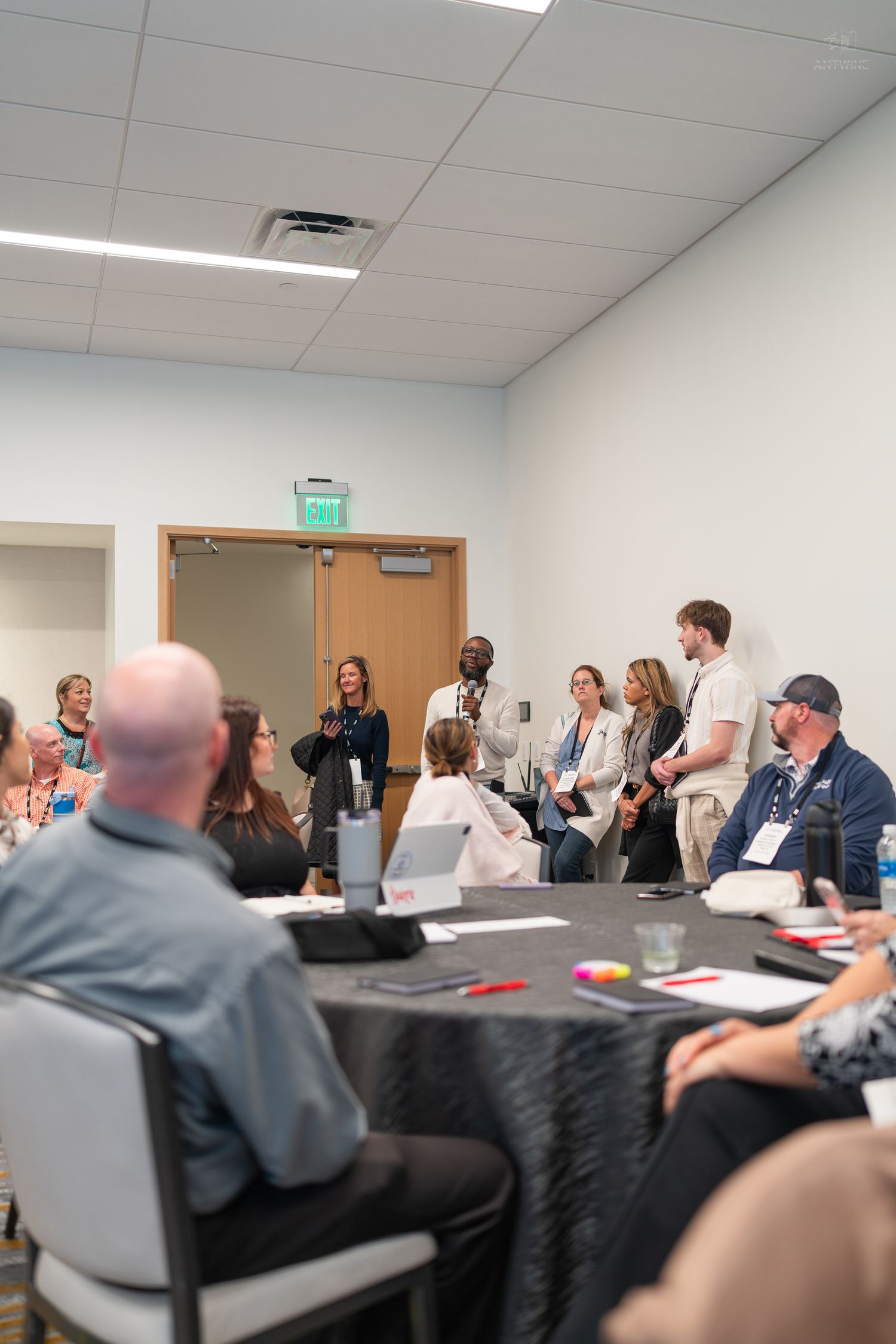 Group of conference attendees standing and presenting in a modern meeting room with round tables.
