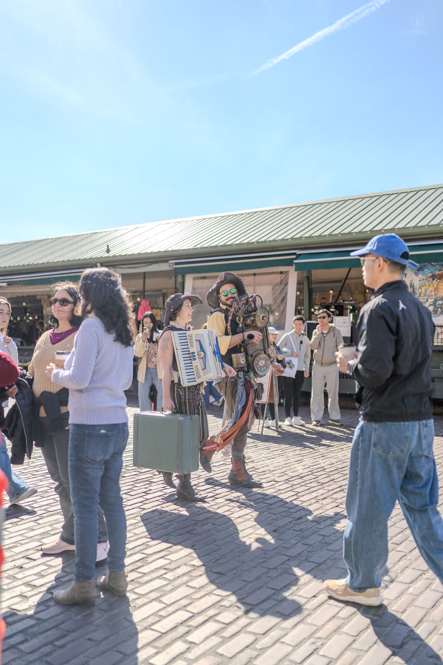 Street performer playing accordion entertaining a crowd of tourists at Seattle's Pike Place Market on a sunny day.