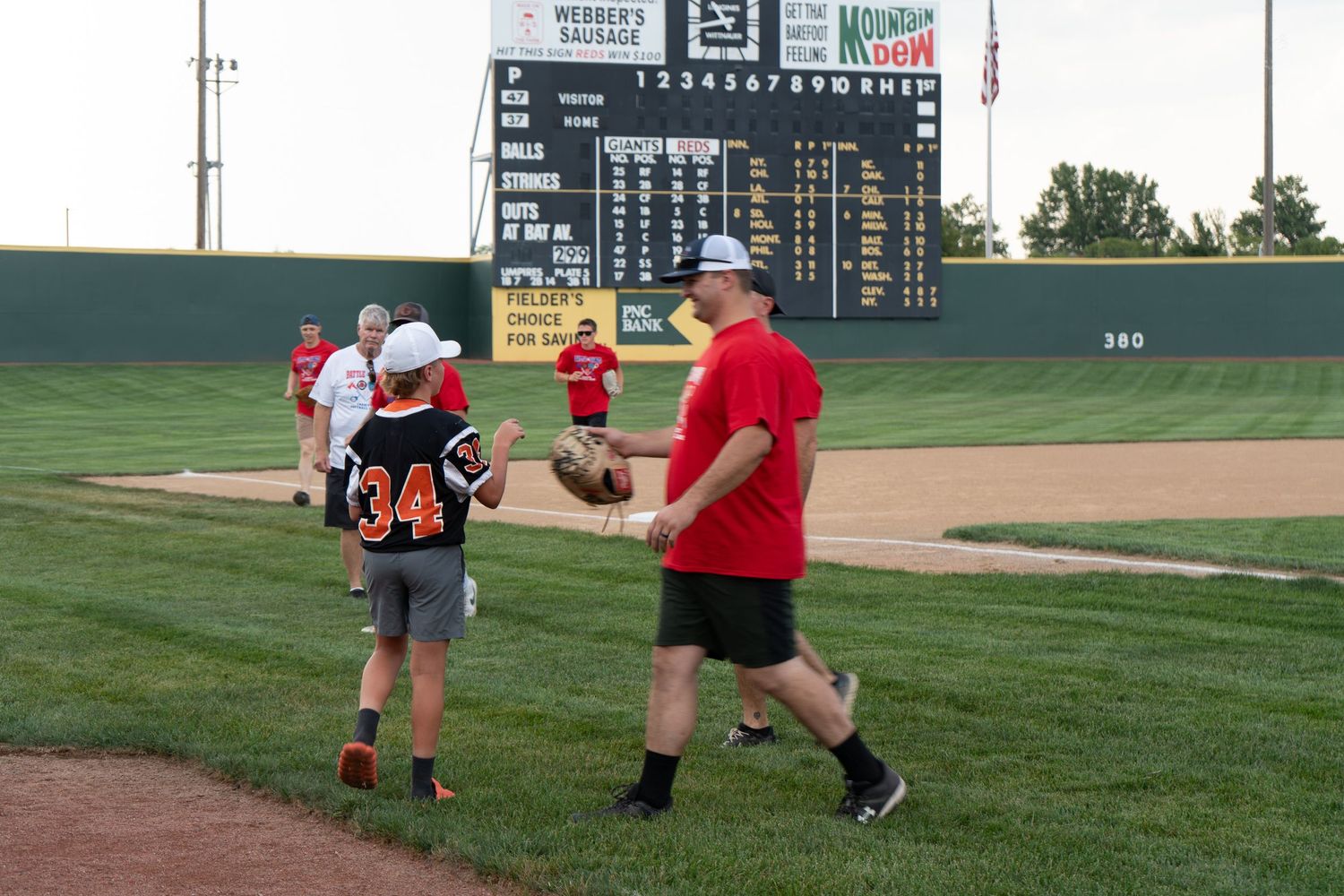 Players exchange a baseball on a green field during an evening recreational softball game at a stadium.