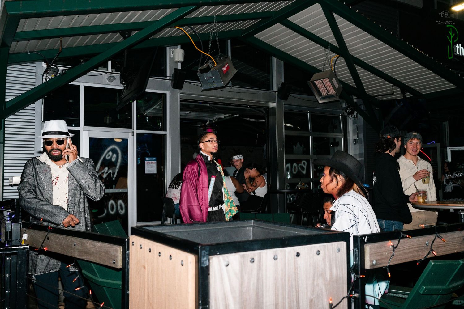 Group of people socializing at an outdoor covered bar venue with string lights.