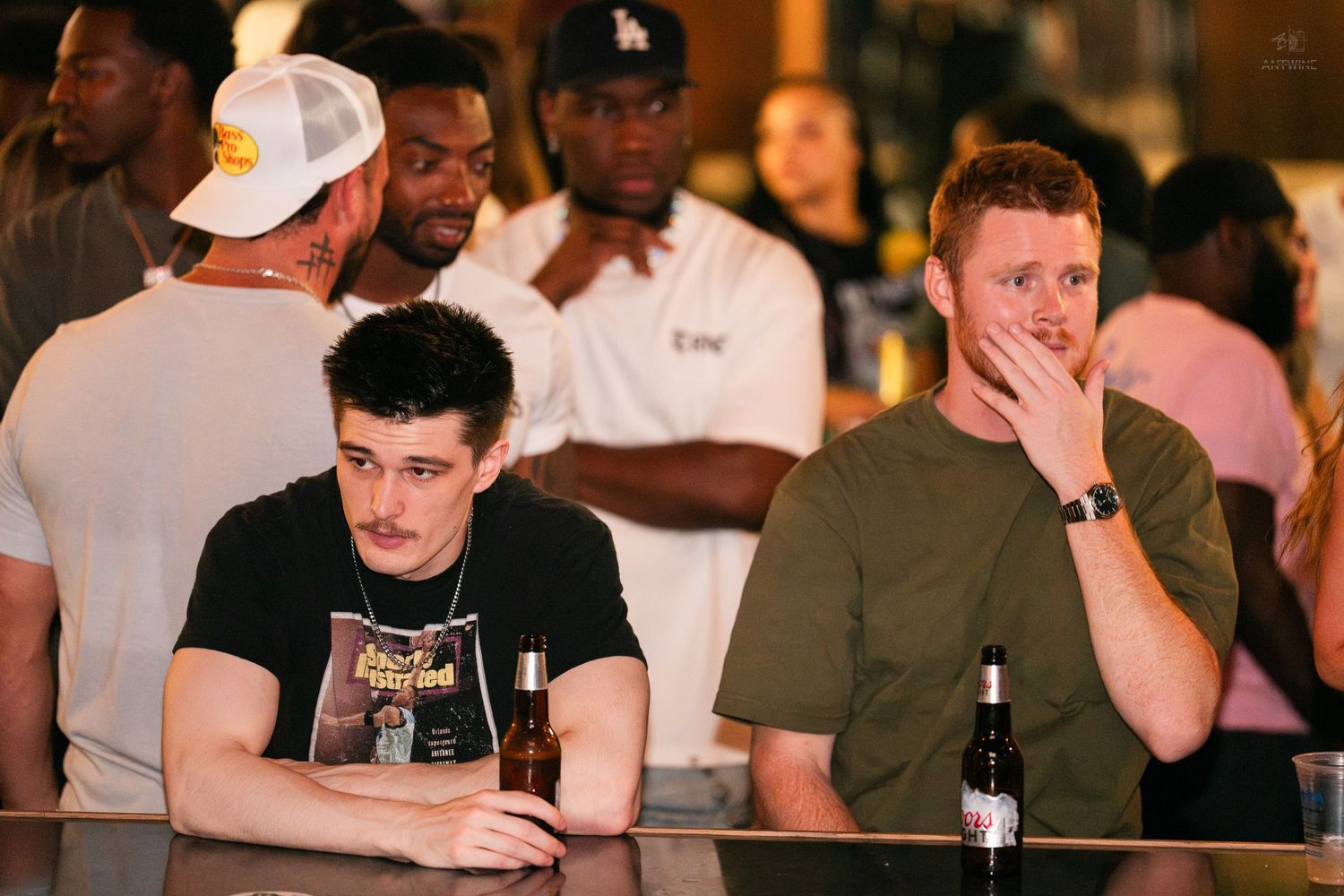 Two young men sitting at a bar counter in a crowded nightclub setting at night.