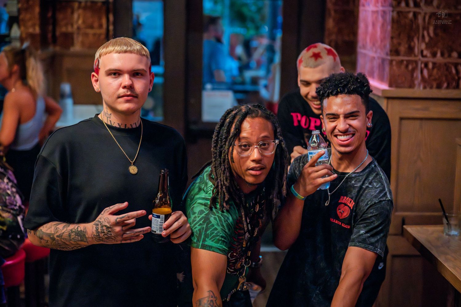 Group of young friends posing together at a bar, holding drinks and smiling at the camera.