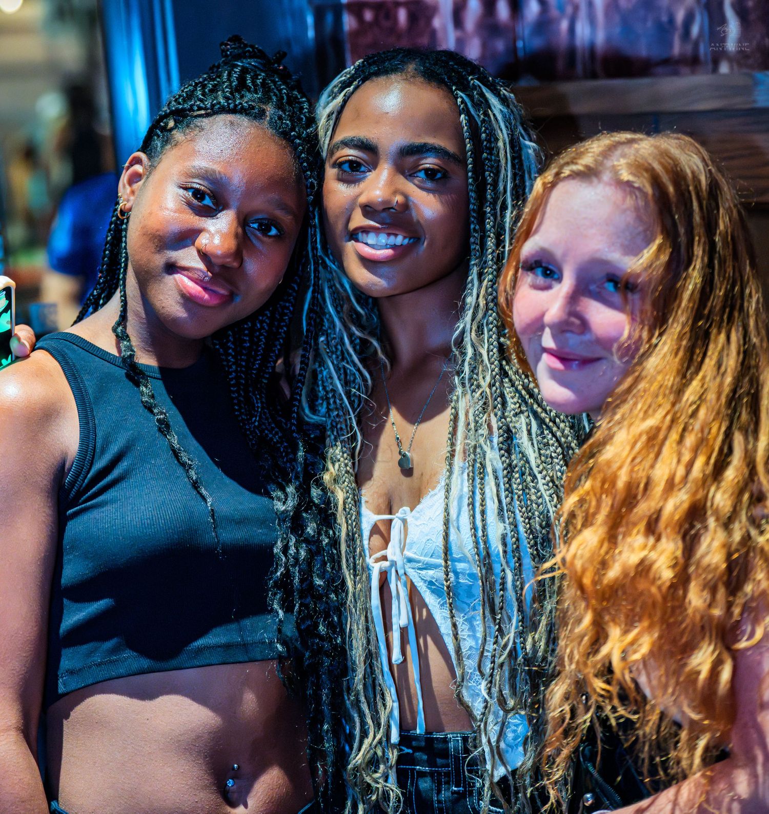 Three young women posing and smiling together at a lively nightclub.