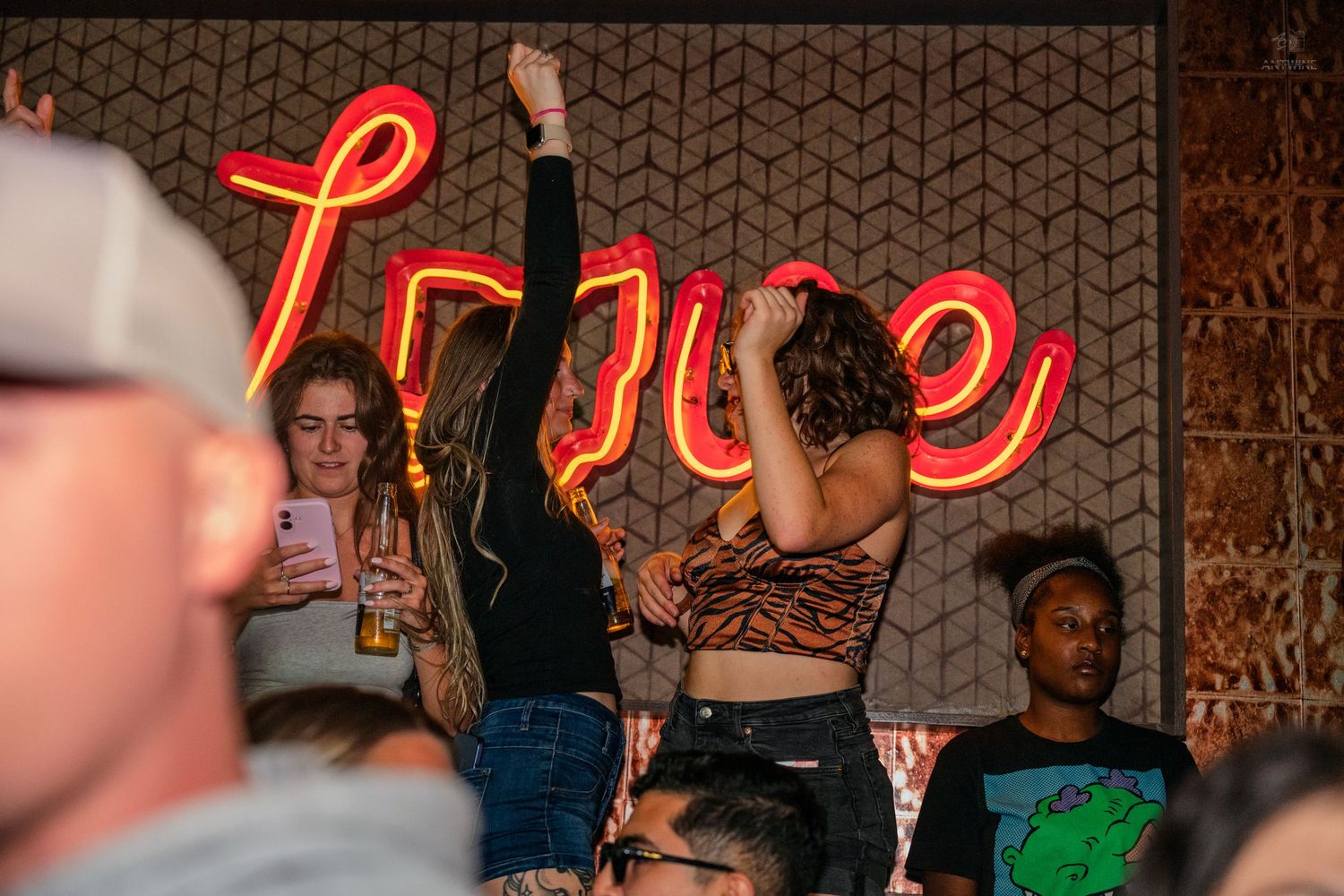 Women dancing and raising hands at a nightclub under a glowing neon sign.