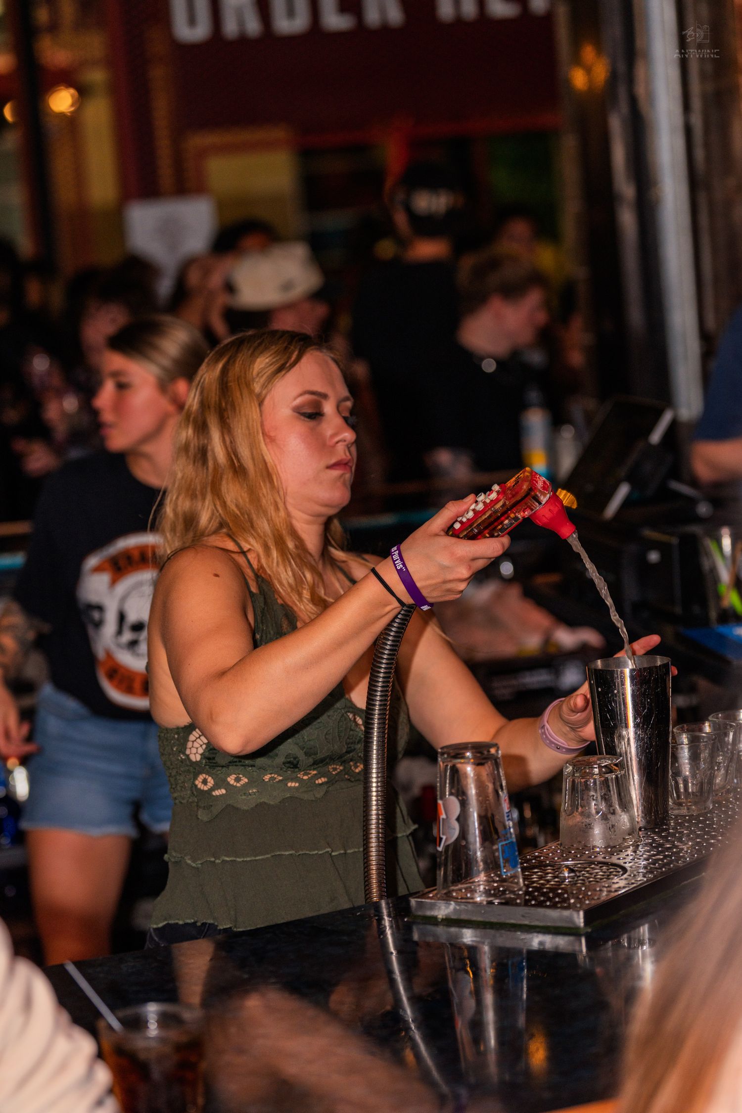 Blonde bartender pouring drinks at a bustling nightlife venue.