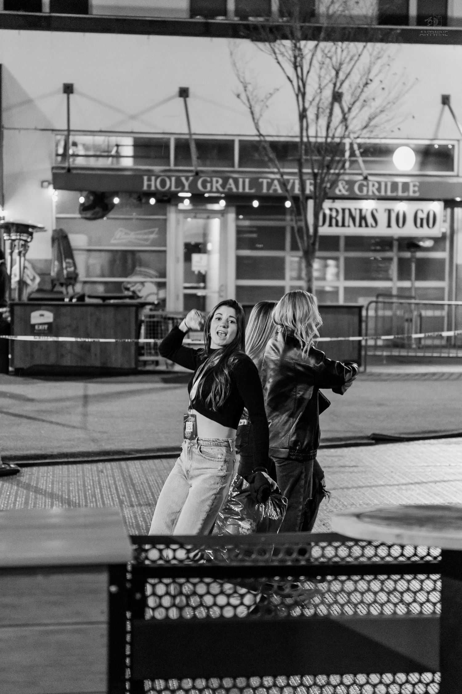 Two women pose for a selfie outside Holy Grail Tavern and Grille at night.